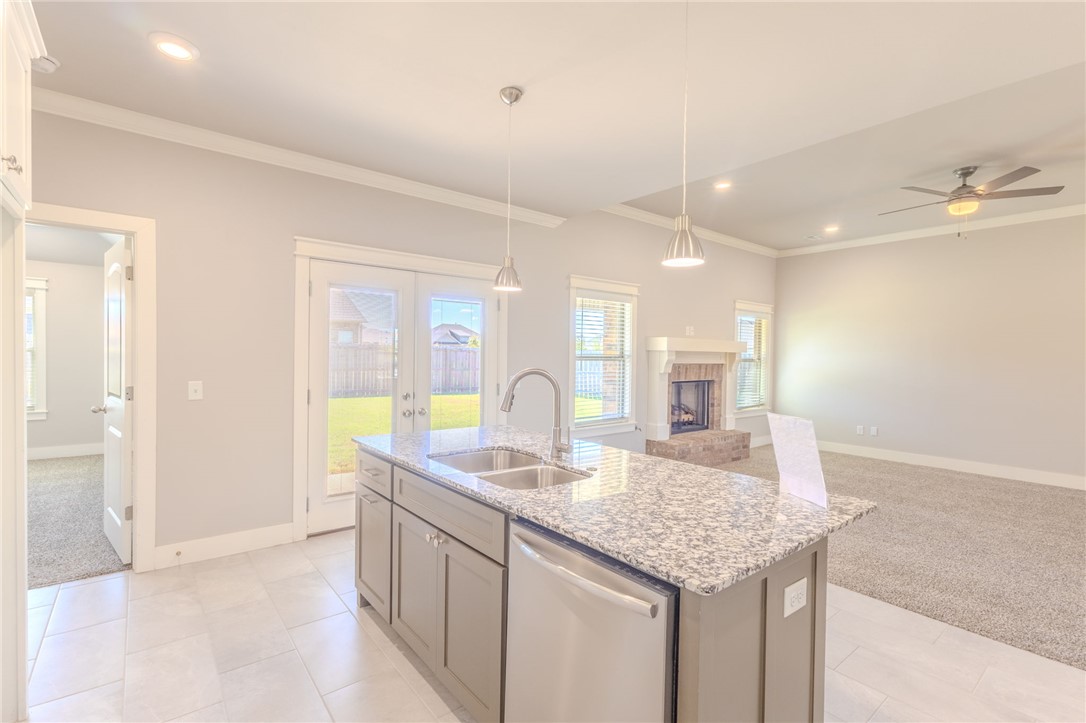 Open-plan kitchen with a granite island, stainless dishwasher, fireplace, and French doors to the backyard.