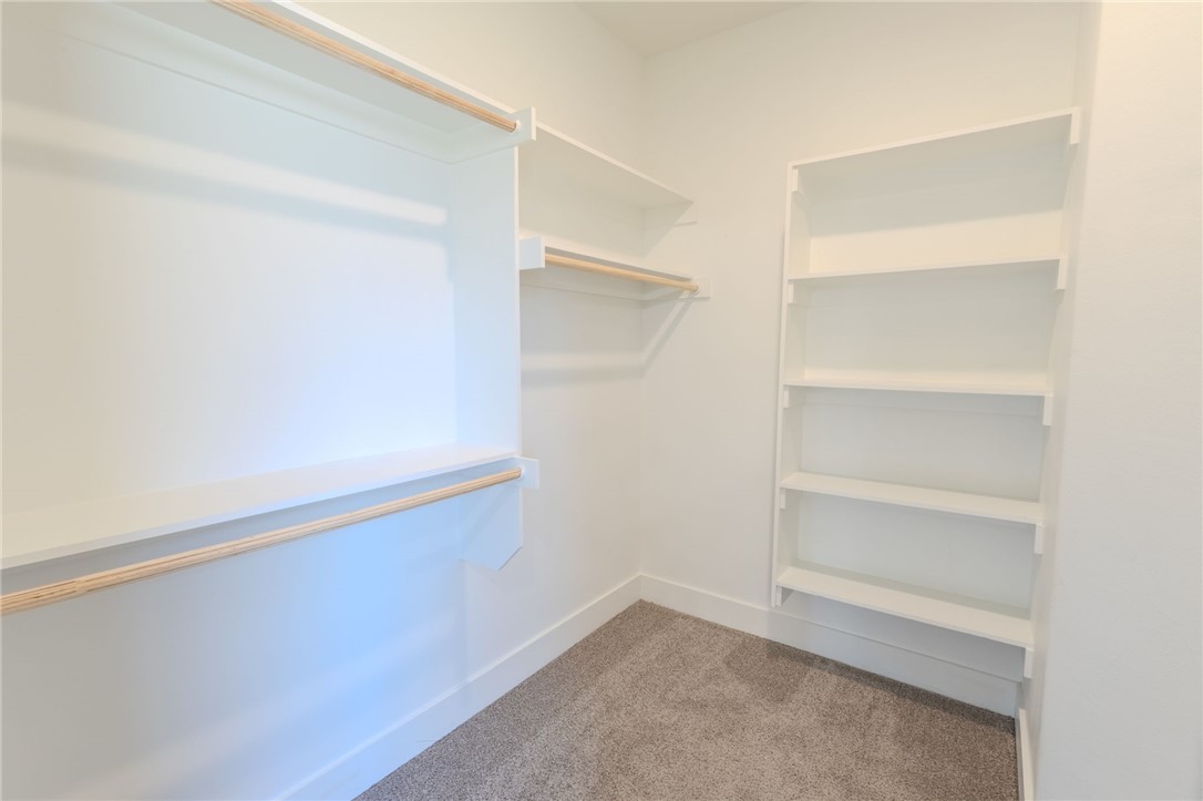Walk-in closet with built-in shelves, wooden hanging rods, and beige carpet.
