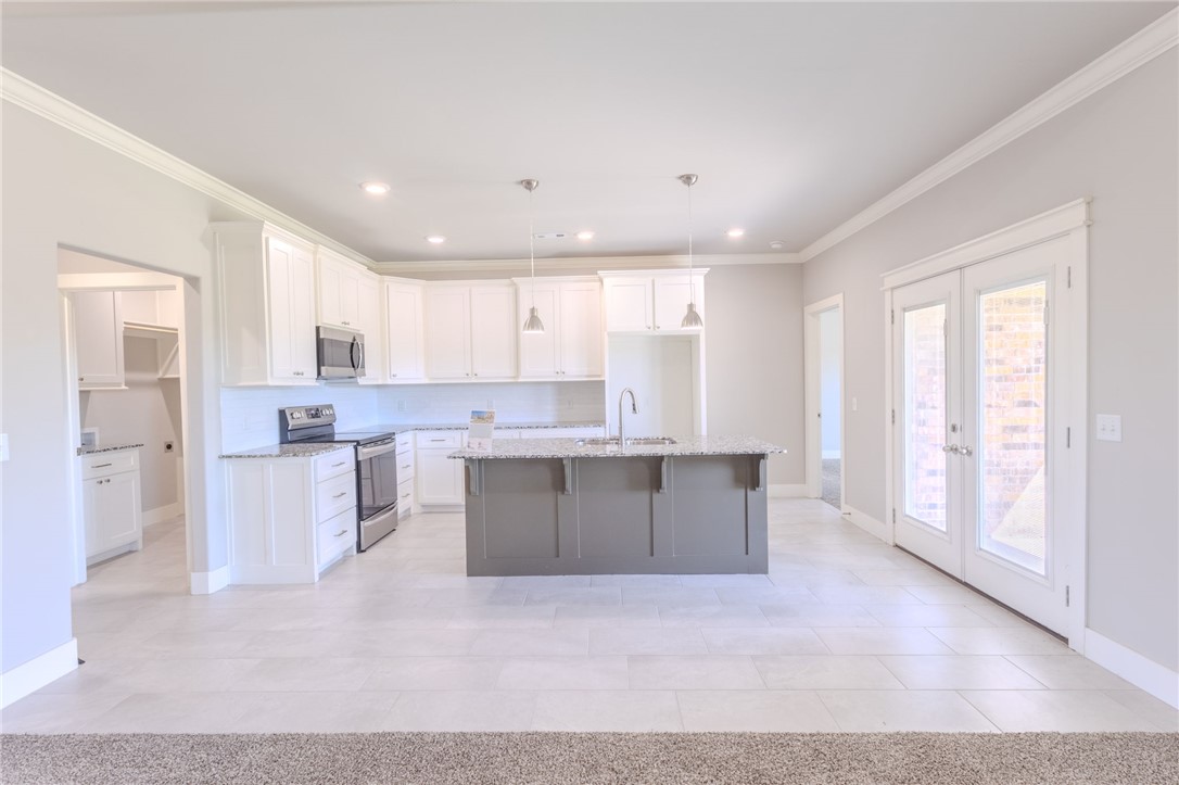 Bright kitchen with white cabinets, stainless appliances, a large gray island, and glass French doors.