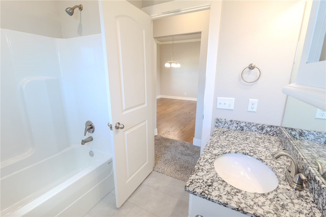 Bathroom with a white tub and shower beside a granite vanity with an oval sink.
