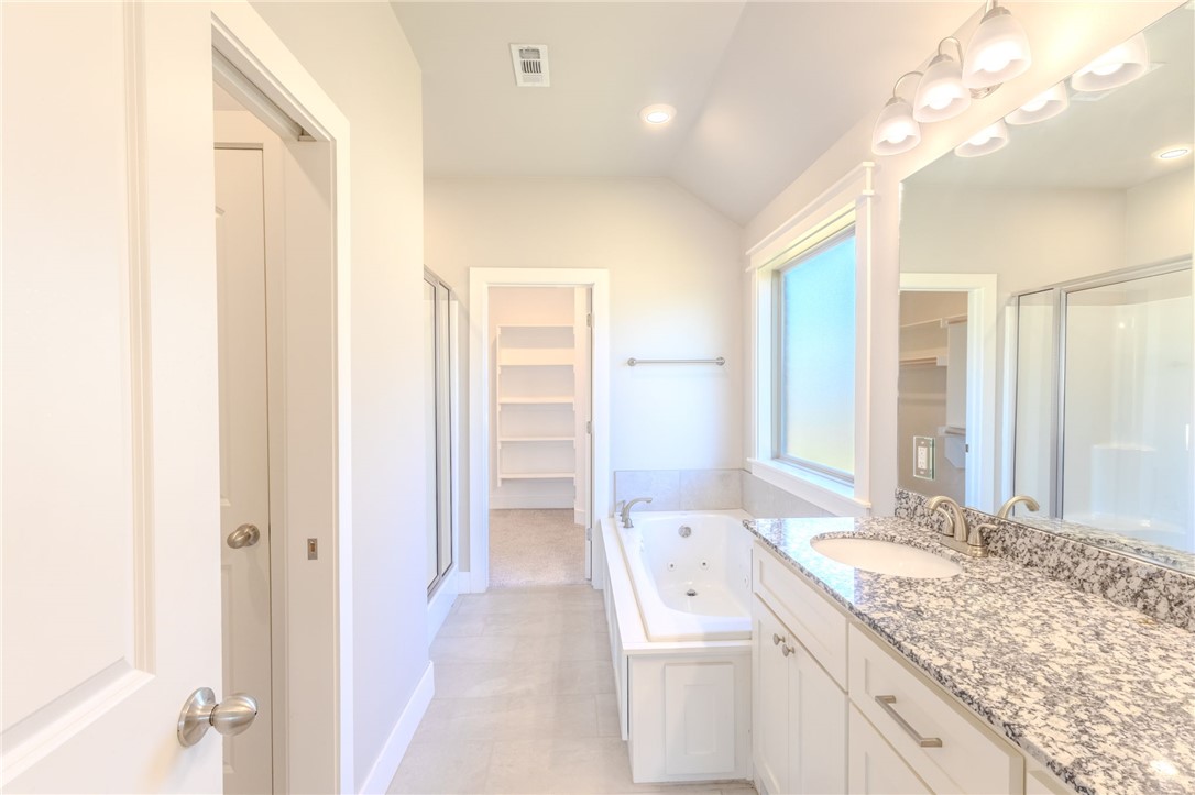 Bathroom with jetted tub, granite double vanity, glass shower, and walk-in closet.