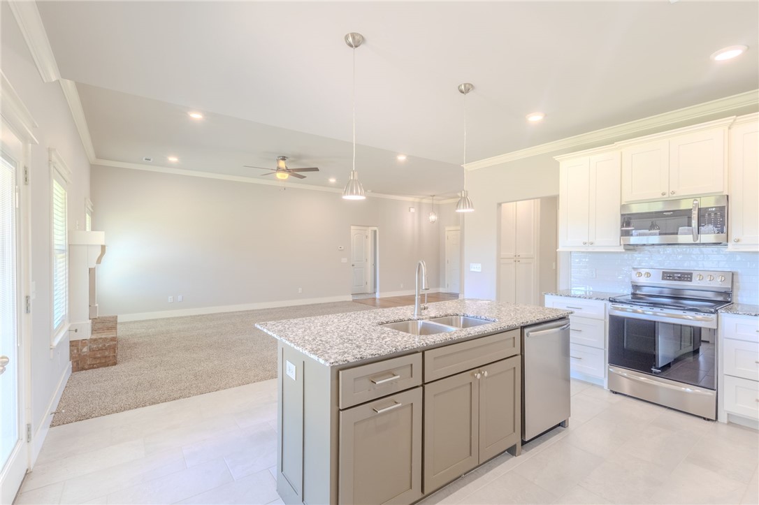 Open-plan kitchen with a large stone island and white cabinets adjoining a carpeted living area.