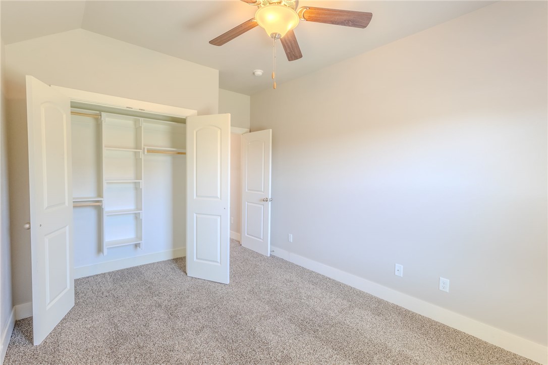 Empty bedroom with an open, built-in closet and a ceiling fan with light.