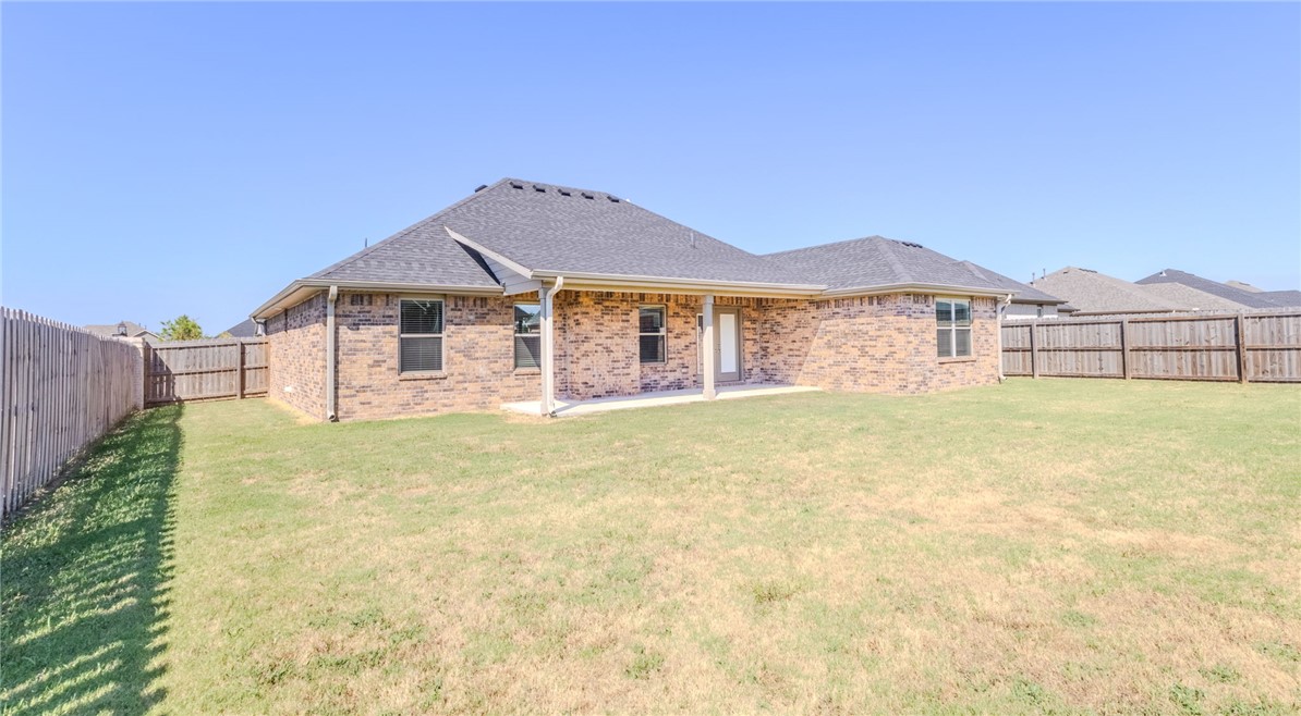 Brick home's rear exterior with a covered patio, grassy backyard, and wooden privacy fence.