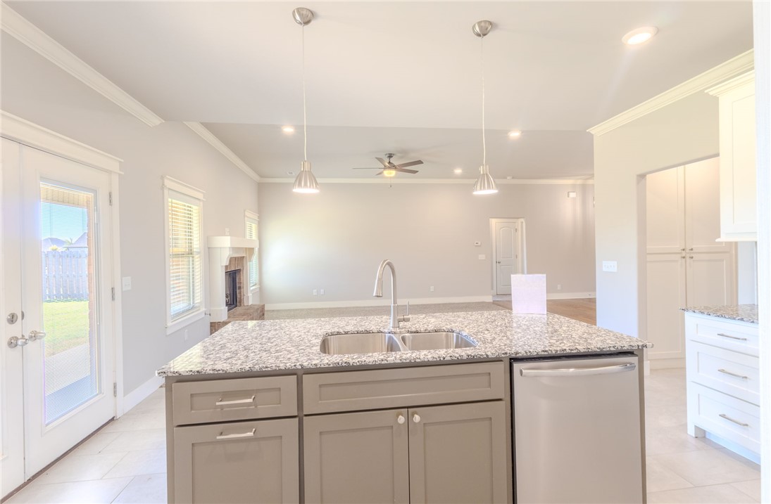 Kitchen with a granite island, double-basin sink, and stainless steel dishwasher opening to a living area.