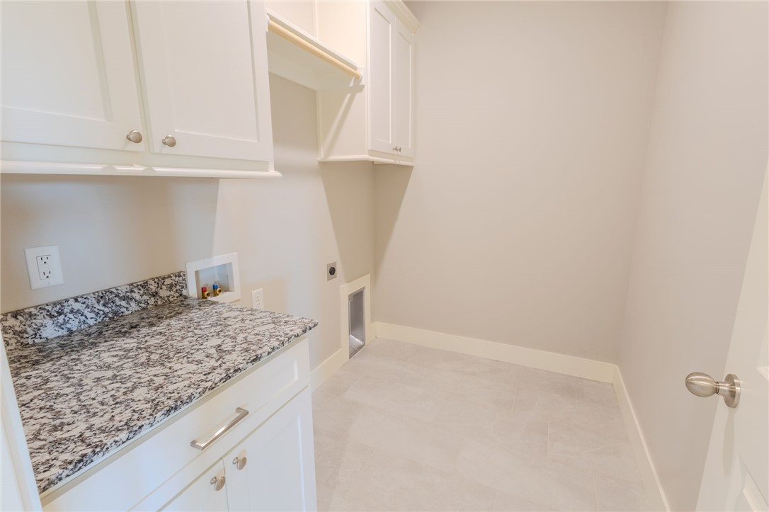 Empty laundry room with white cabinets, granite countertop, and washer and dryer hookups.