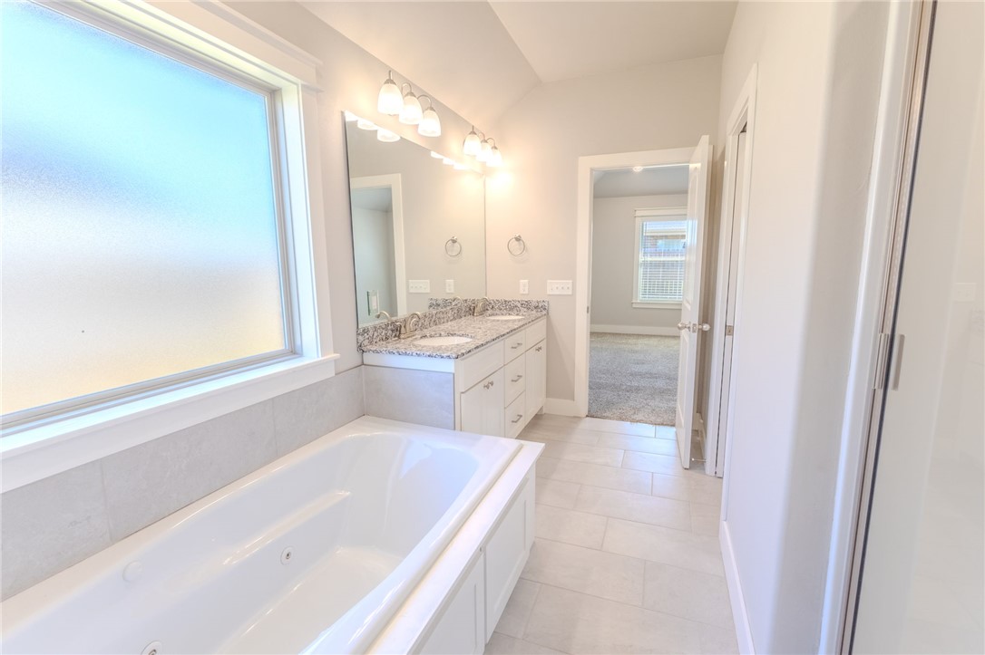 Bathroom with a built-in soaking tub beside a frosted window and a granite-topped vanity.