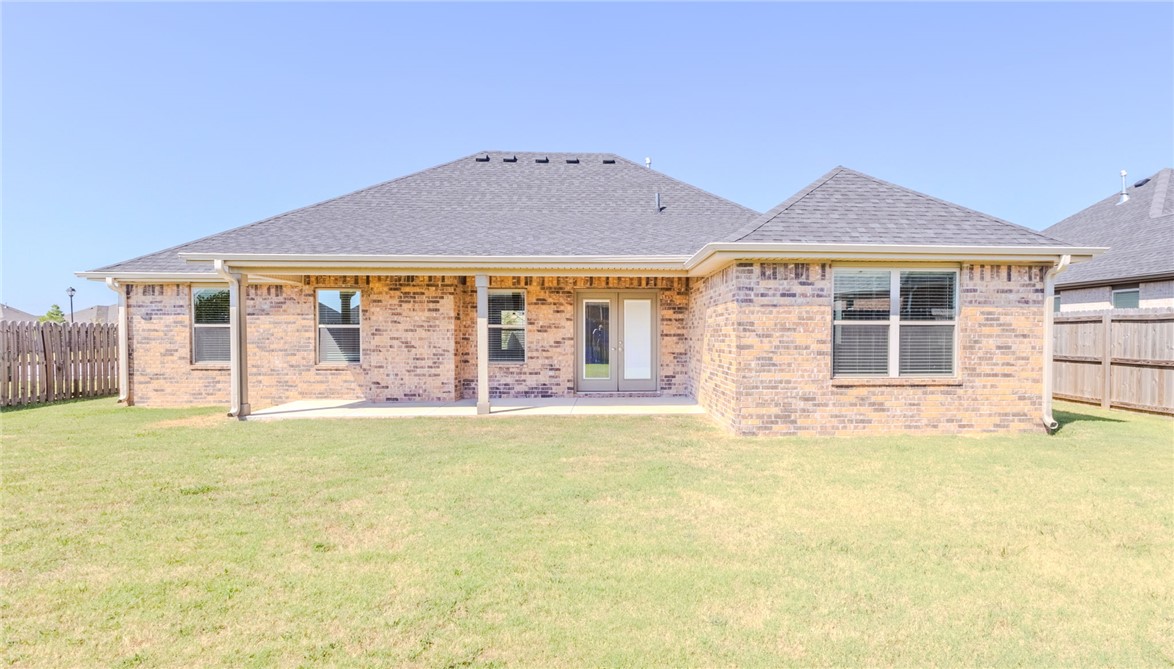 Brick home’s rear exterior with a covered patio, fenced yard, and broad lawn.