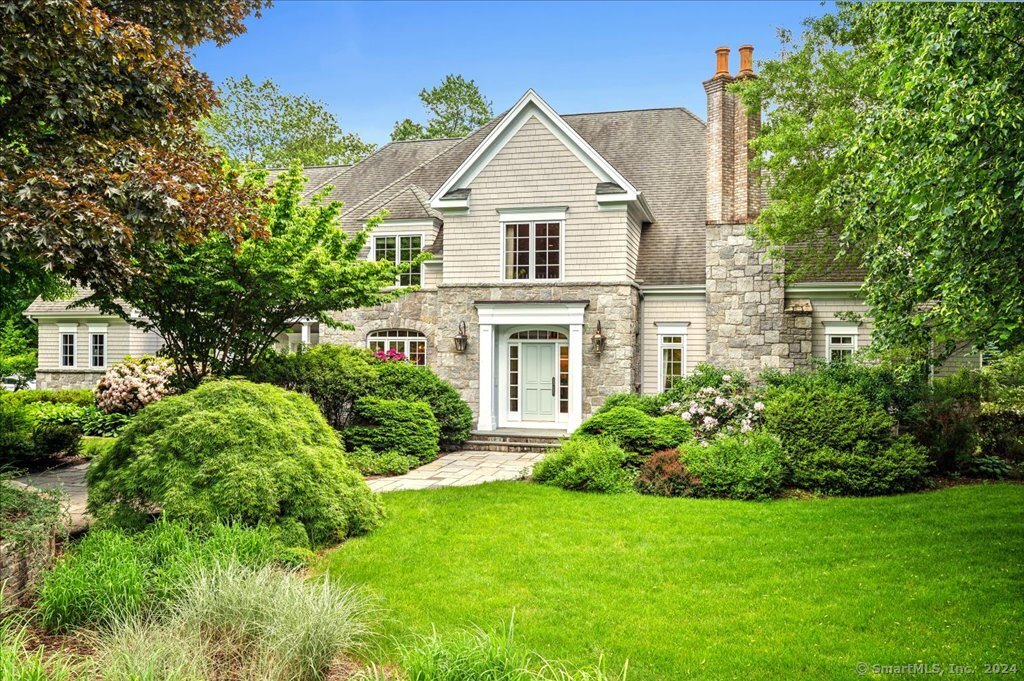 Stone-and-shingle home with twin chimneys, a central front entry, and landscaped gardens.