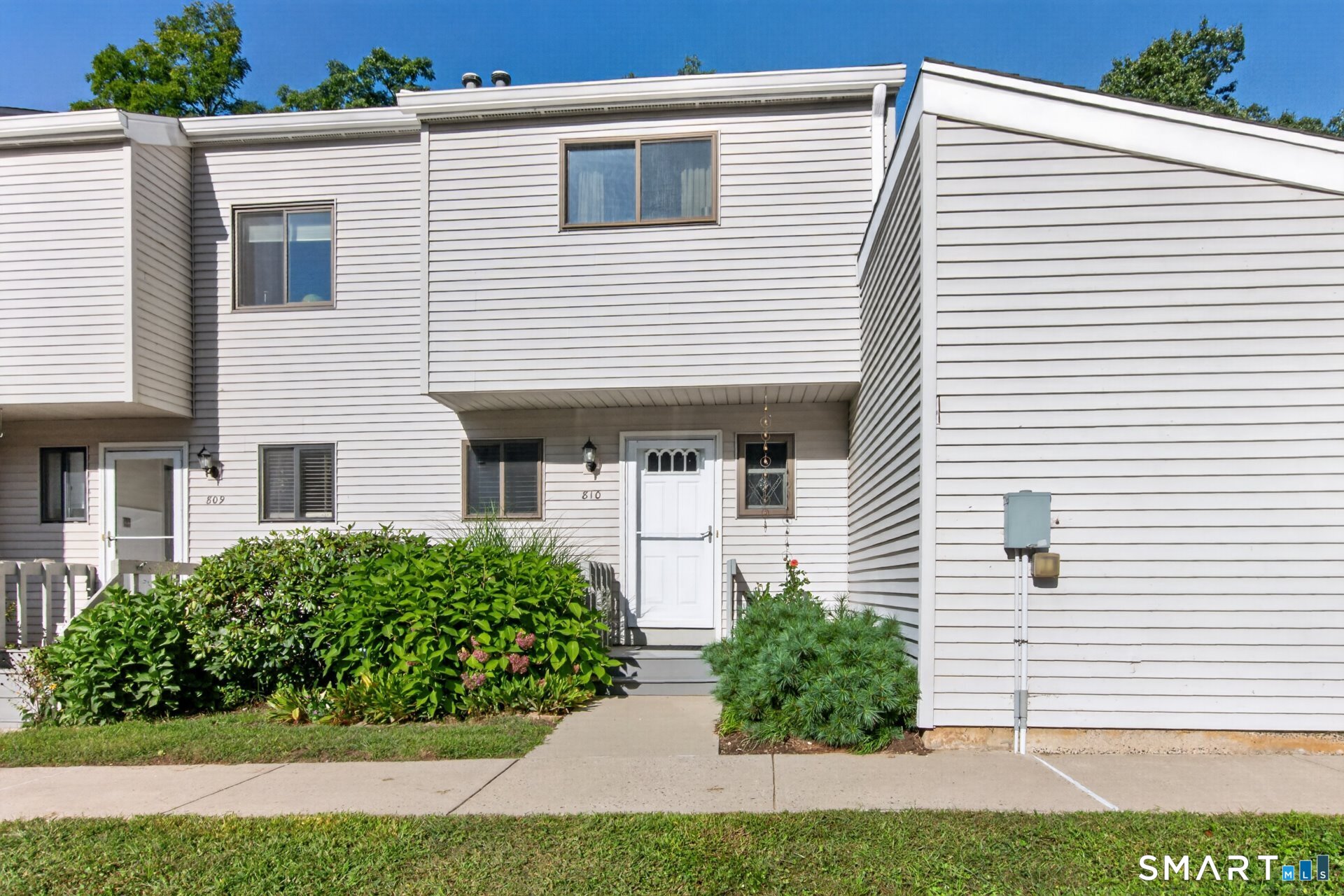 White-sided townhouse entrance marked 810, with a front walkway and leafy shrubs.