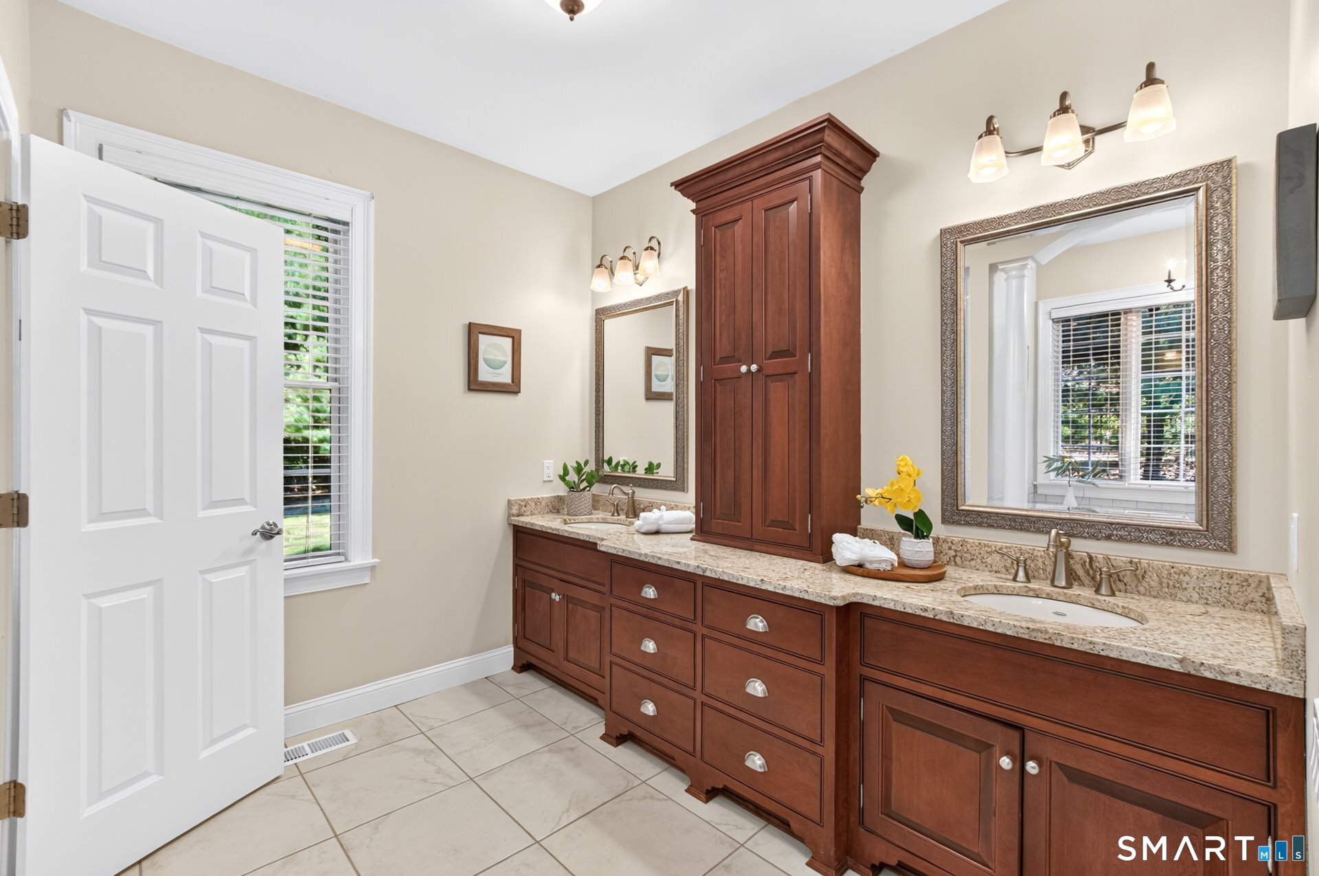 Bathroom with a double-sink vanity, rich wood cabinetry, stone counters, and large framed mirrors.