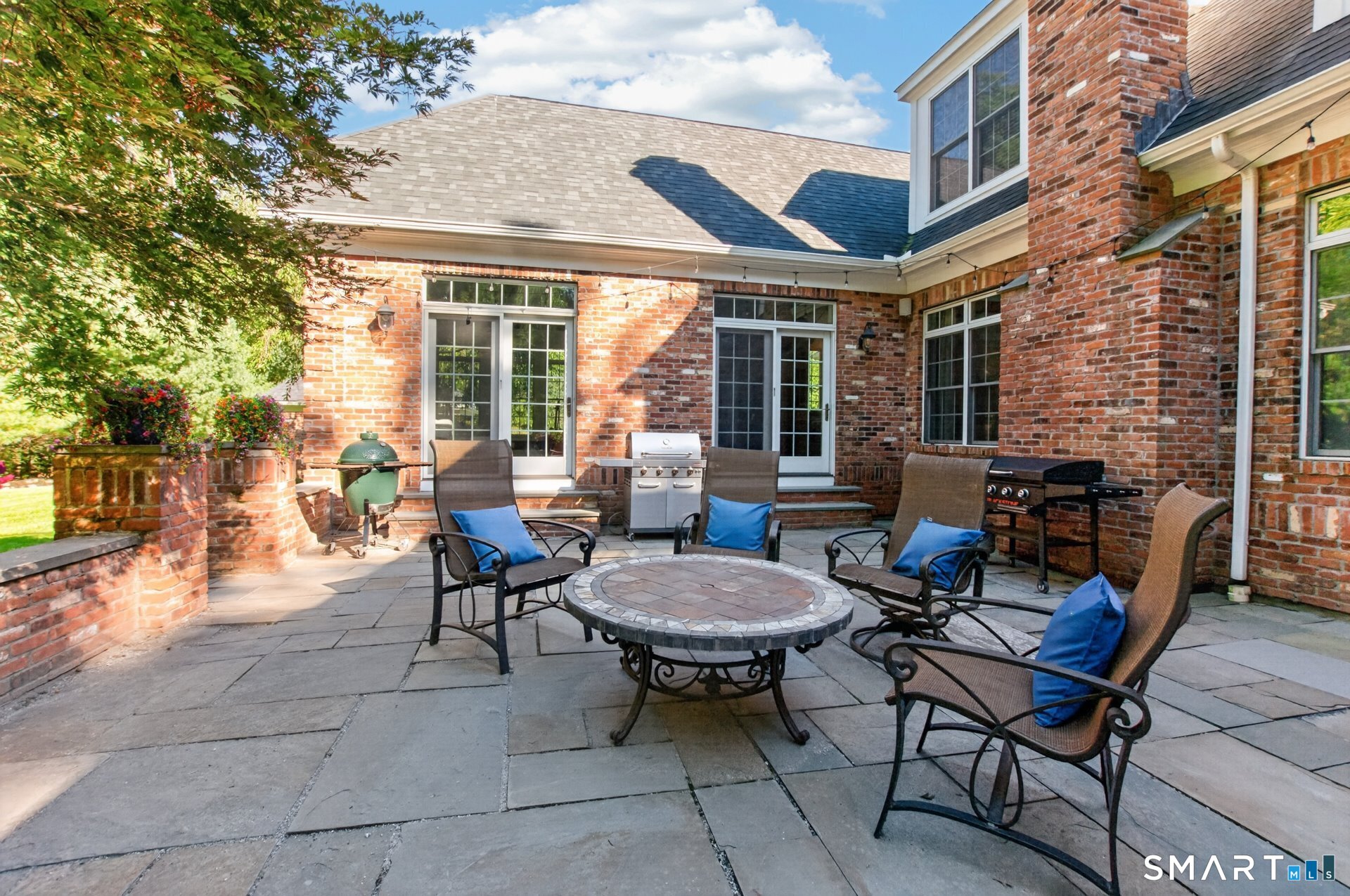 Brick home’s furnished stone patio with a round table, chairs, and two grills.