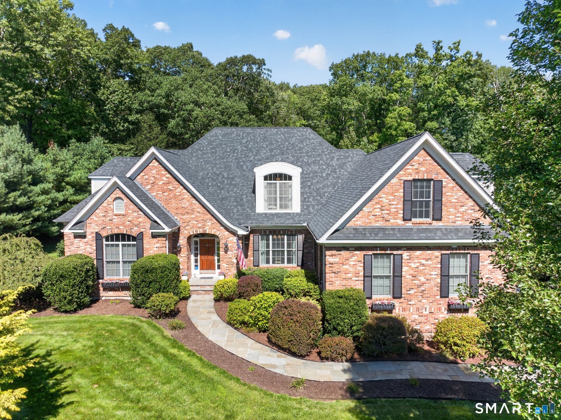 Red-brick home with a gray roof, landscaped shrubs, and a curved stone walkway.