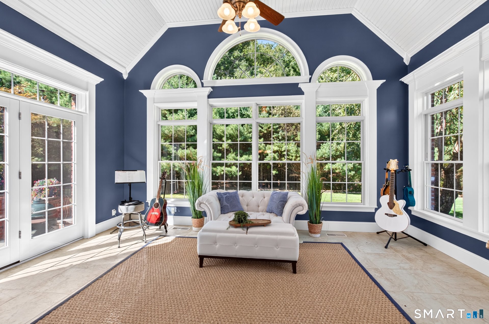 Furnished sunroom with arched windows, navy walls, a white sofa, and guitars.