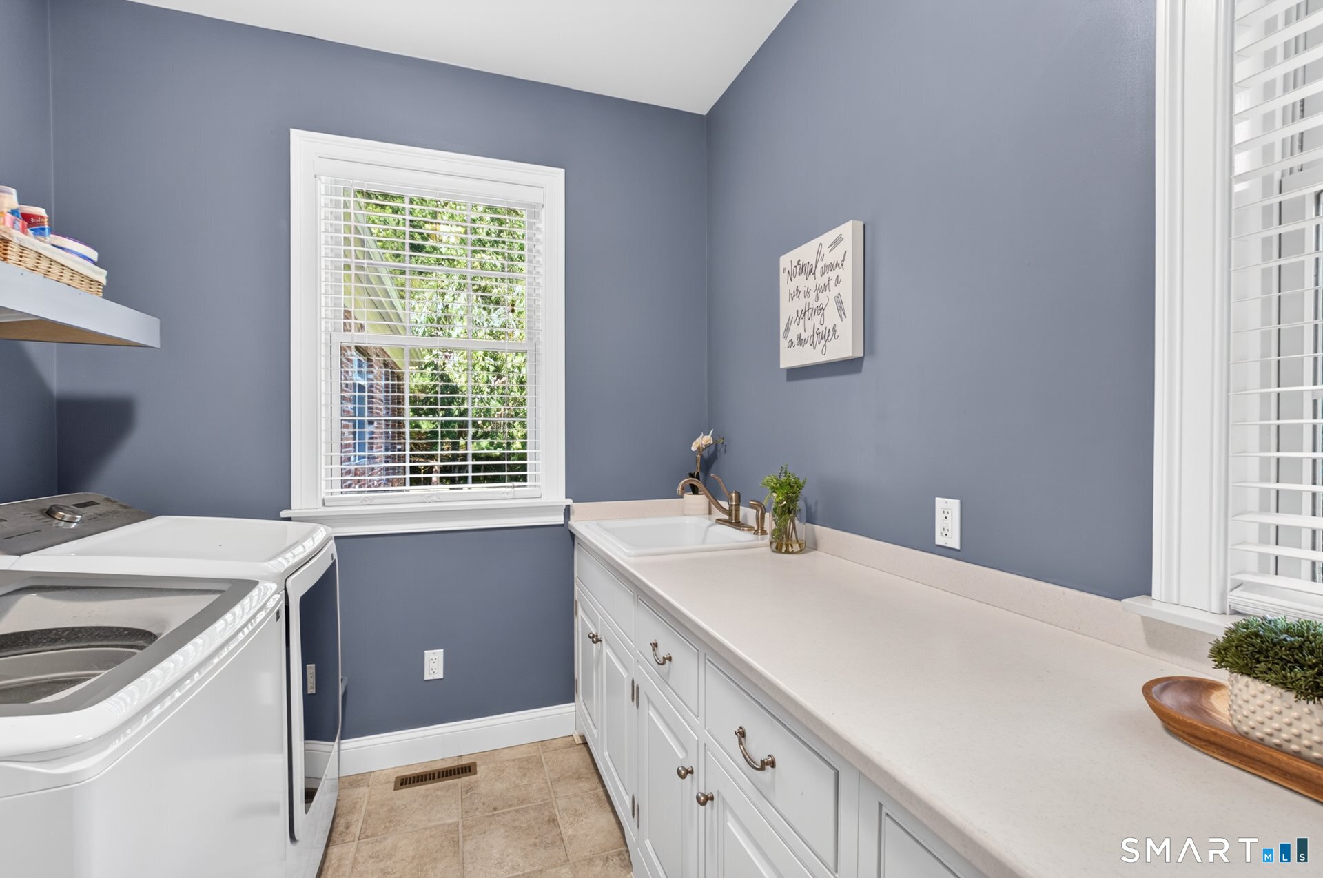 Laundry room with white washer and dryer, long countertop, utility sink, and blue walls.