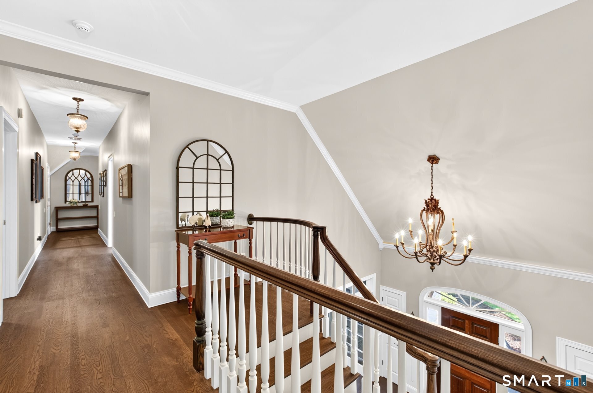 Upstairs hallway and stair landing with hardwood floors, a dark wood railing, and an ornate chandelier.