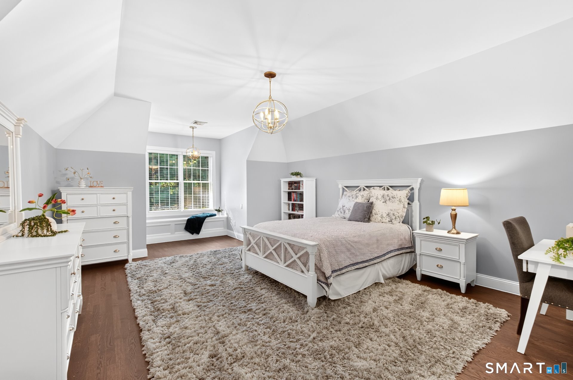 Bedroom with vaulted ceiling, white furnishings, window seat, and plush neutral rug.