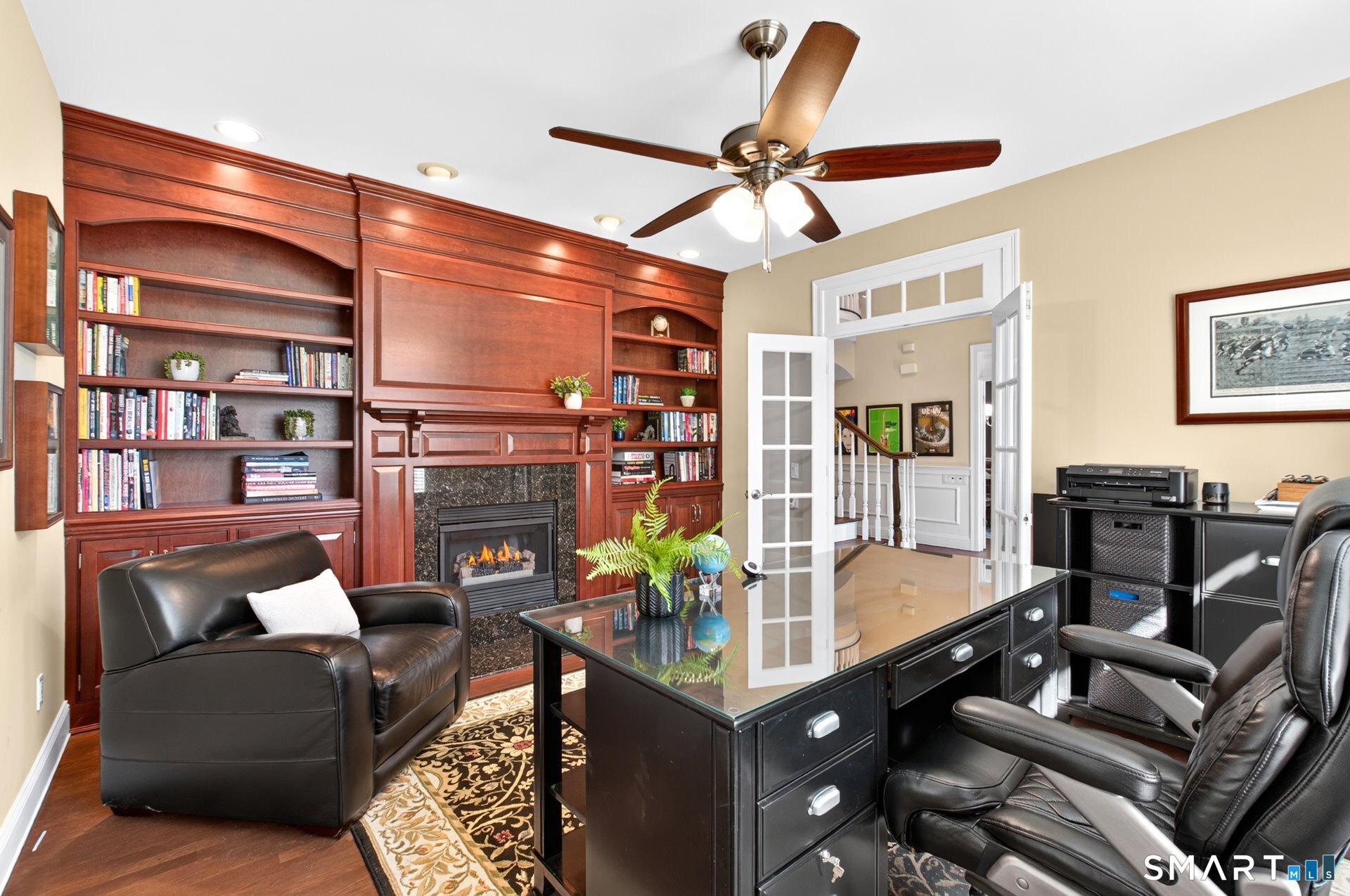 Furnished home office with wood built-ins, a fireplace, glass-top desk, and leather chairs.
