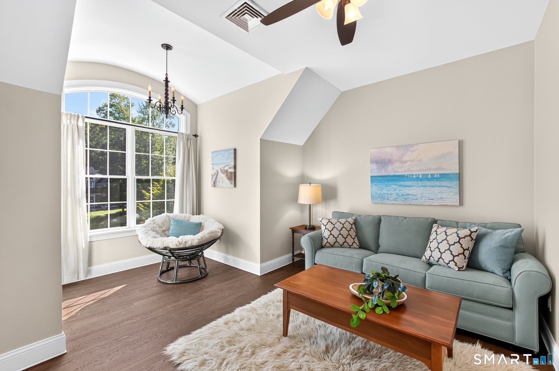 Living room with a vaulted ceiling, arched window, blue-gray sofa, and wicker lounge chair.