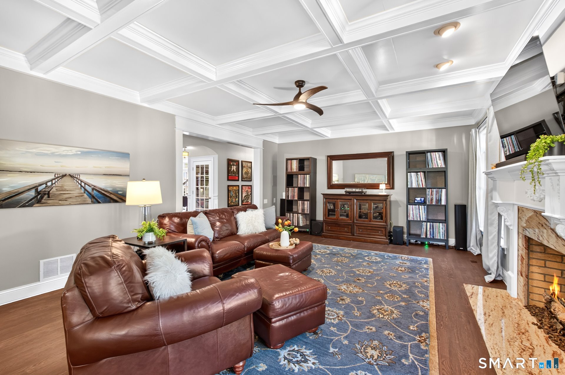 Living room with a coffered ceiling, brown leather sectional, blue patterned rug, and fireplace.