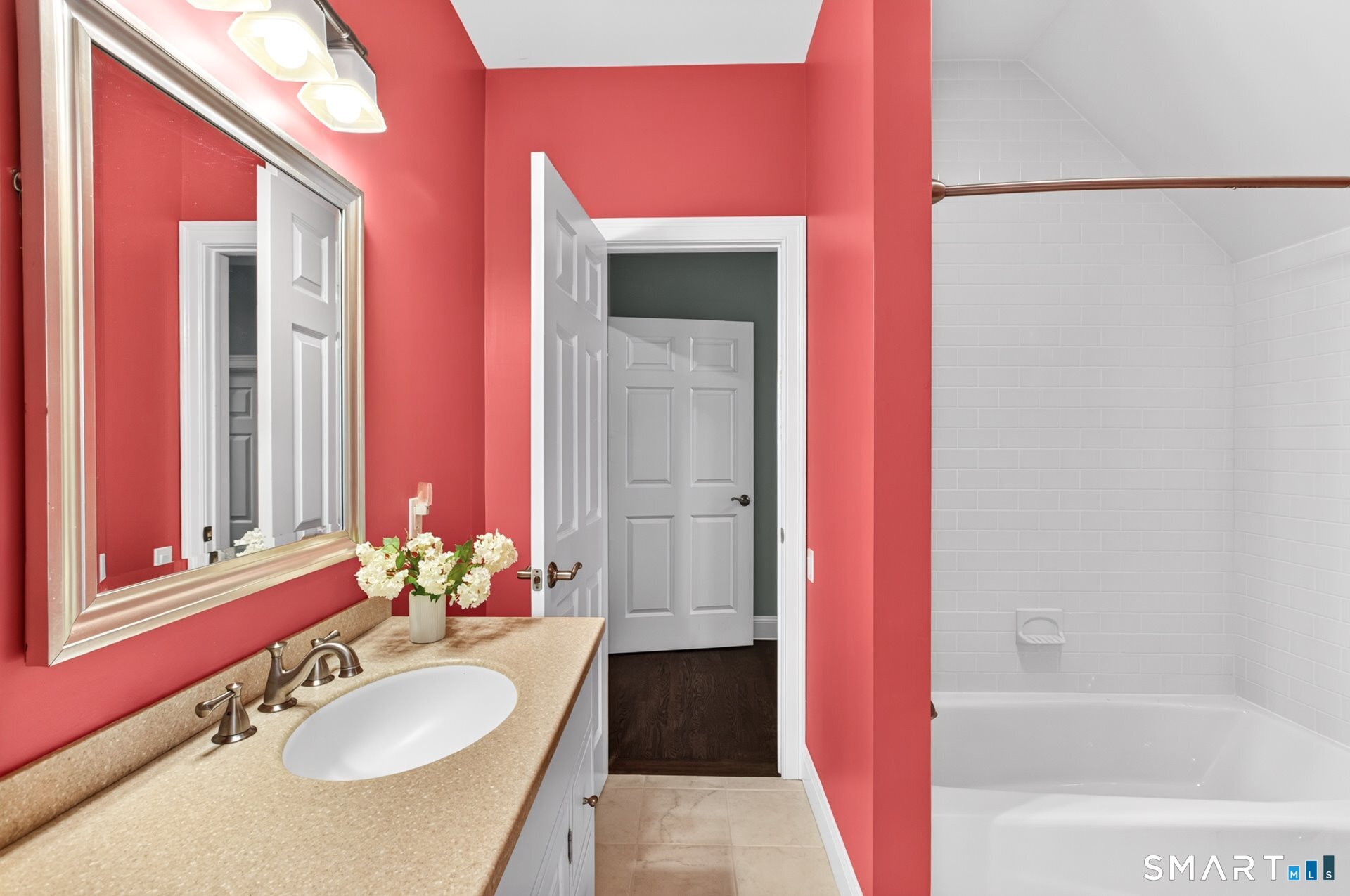 Bathroom with a beige double-sink vanity, coral-red walls, and a white tiled bathtub.
