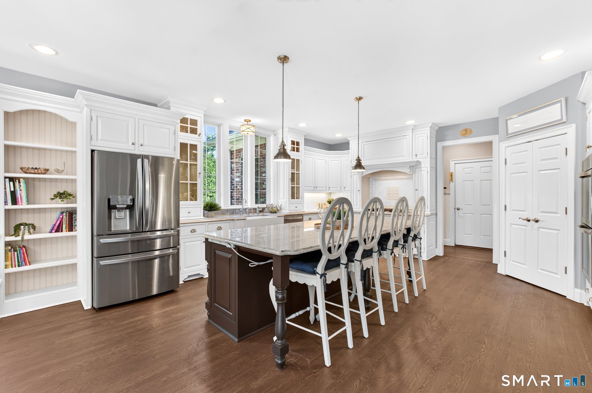 Bright kitchen with white cabinetry, stainless refrigerator, and a large island lined with bar stools.