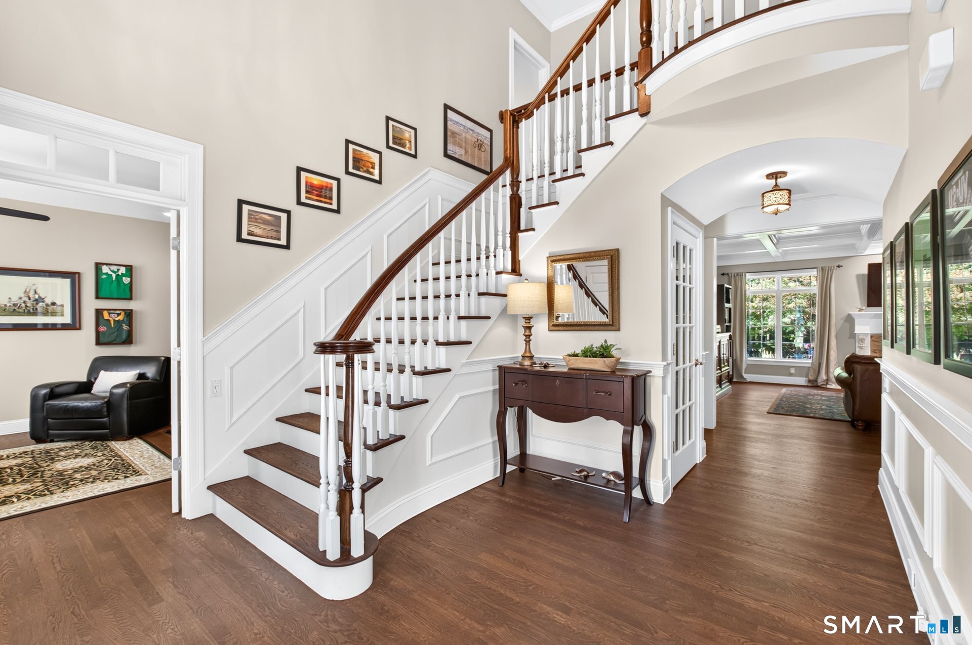 Foyer with a sweeping dark-wood staircase, white balusters, and a console table beneath a mirror.