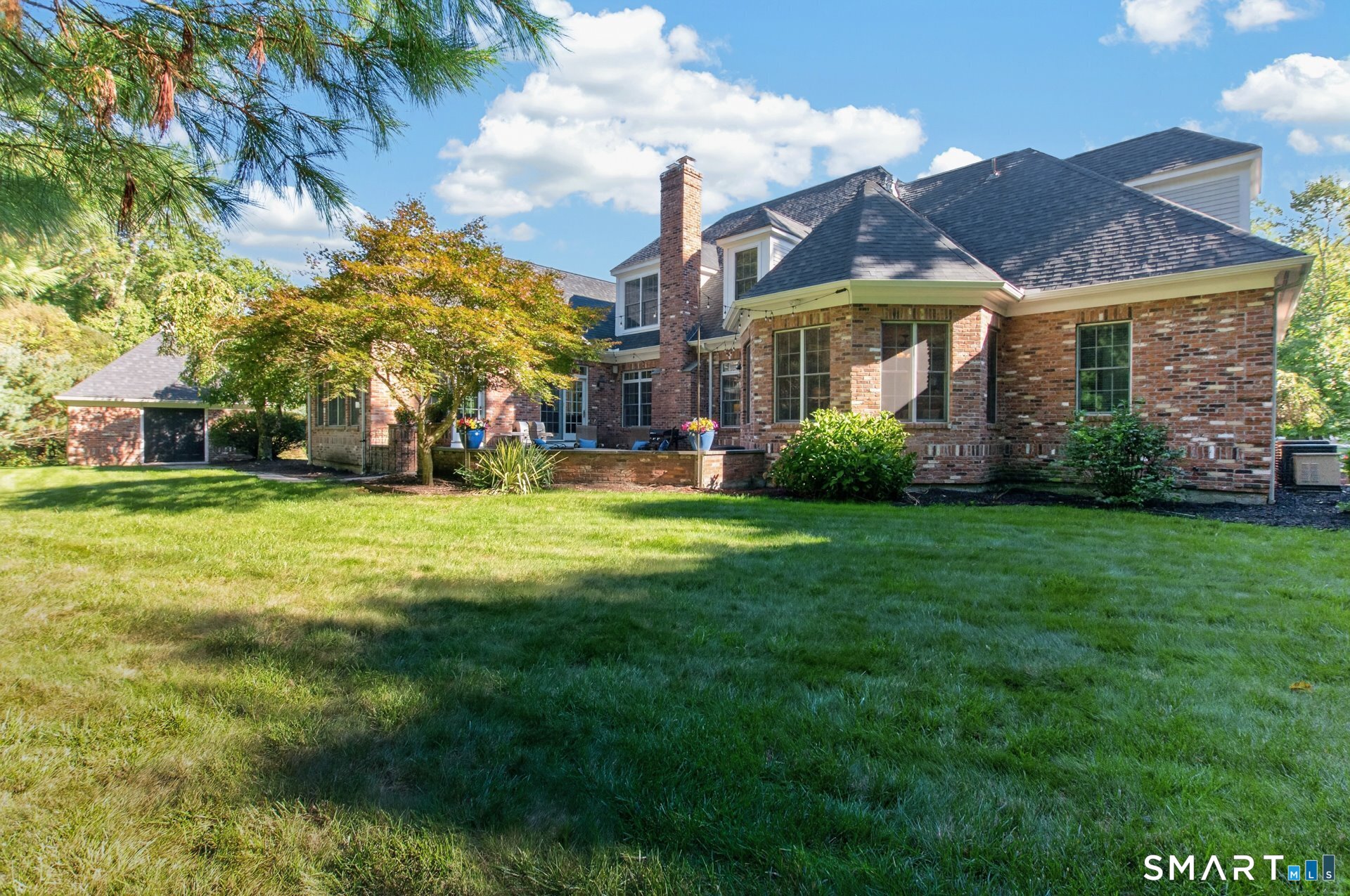 Brick house with a broad lawn, patio, and detached garage.