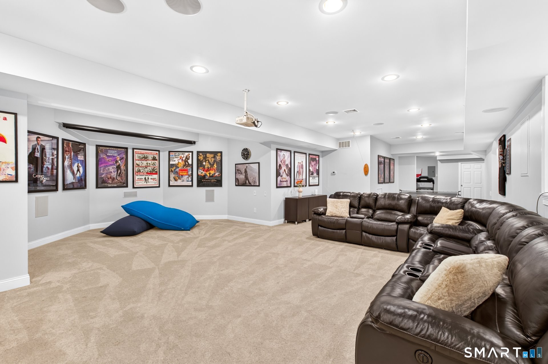 Basement media room with a ceiling projector, movie posters, and a large leather sectional.