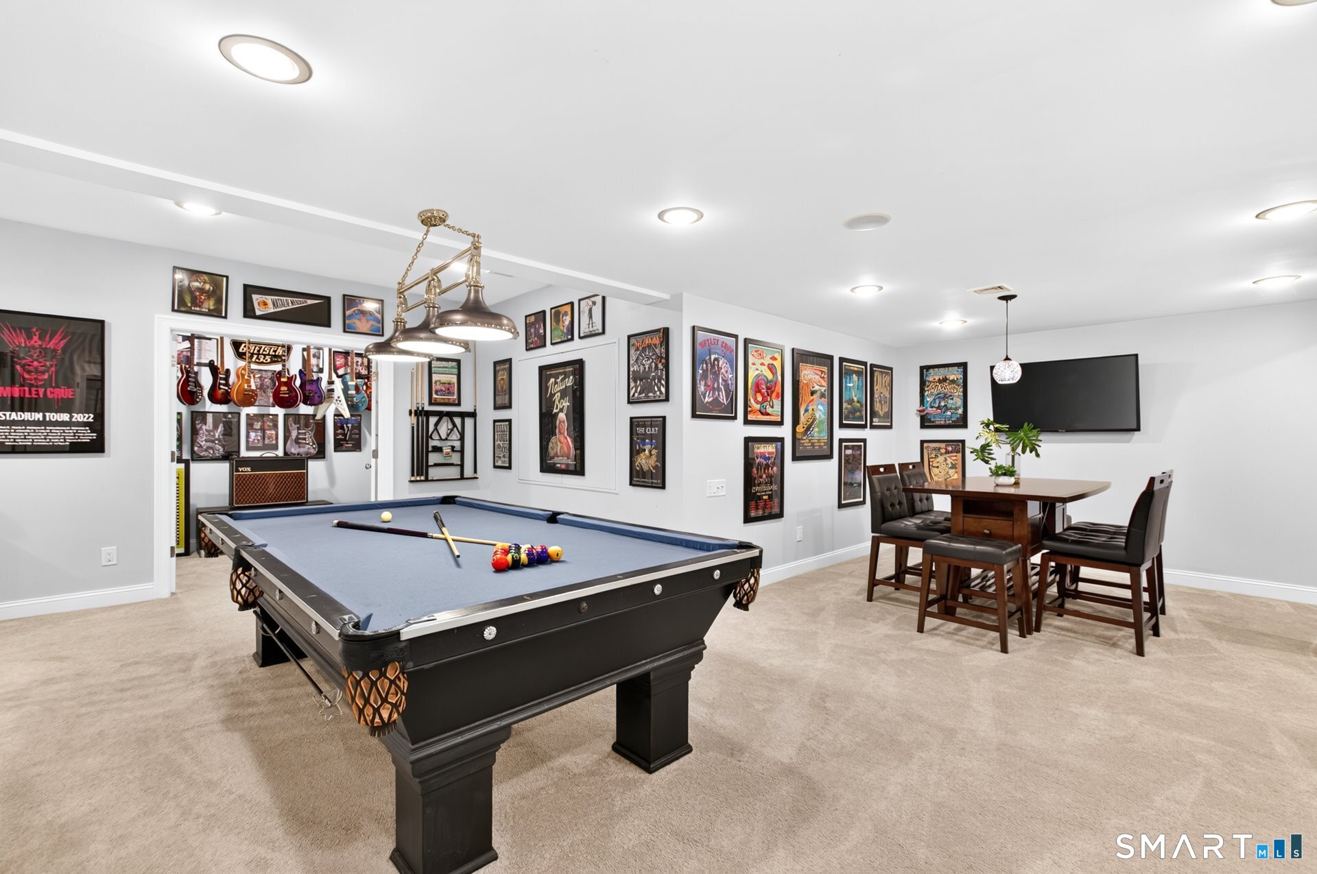 Game room with a pool table, wall-mounted guitars, framed music posters, and a high-top dining table.