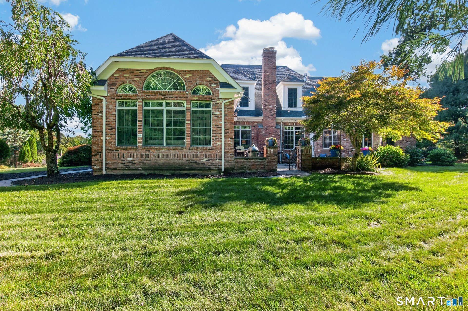 Brick home with an arched-window sunroom, patio seating, and a broad lawn.