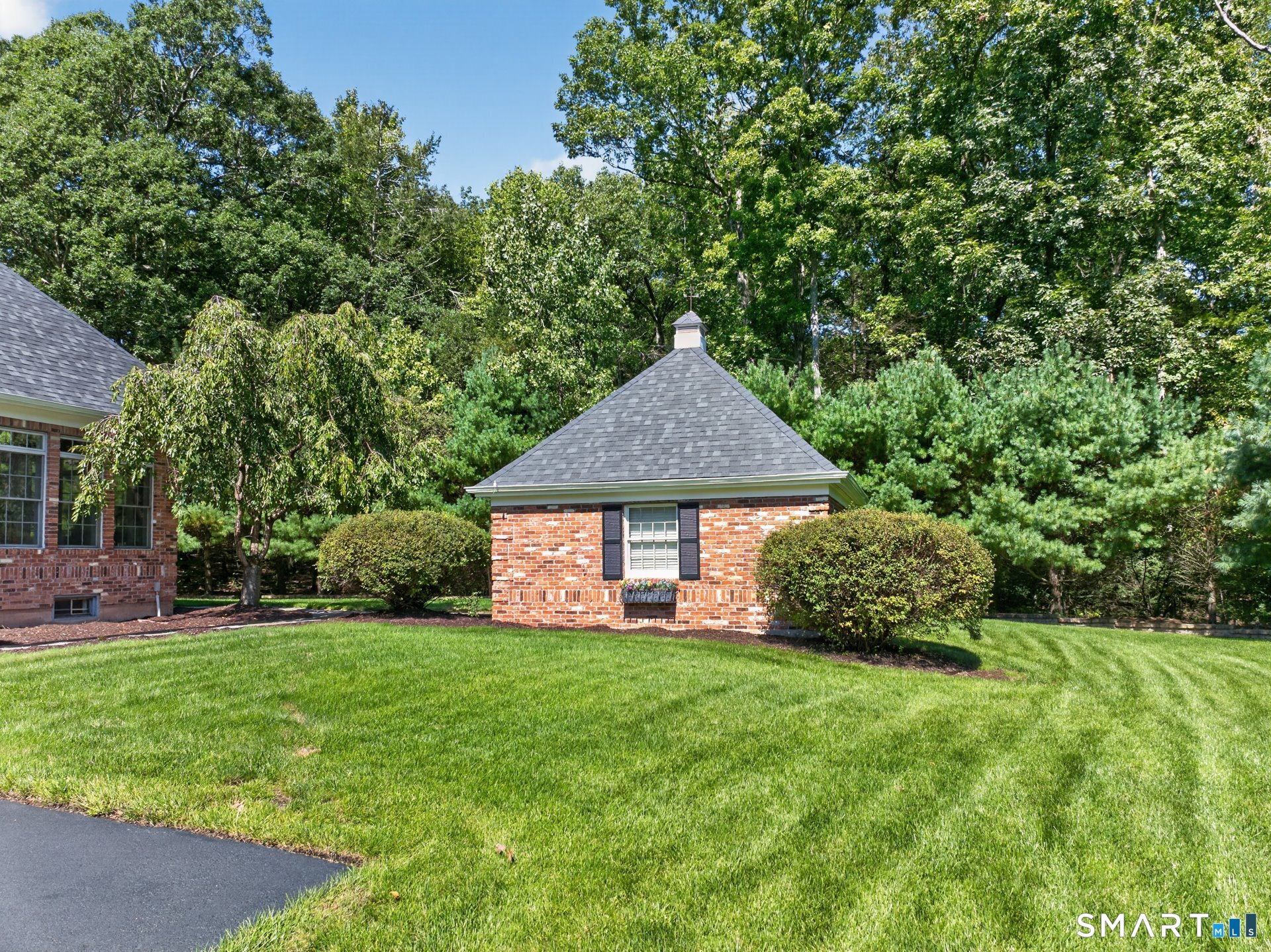 Brick garden pavilion beside a manicured lawn and wooded yard.