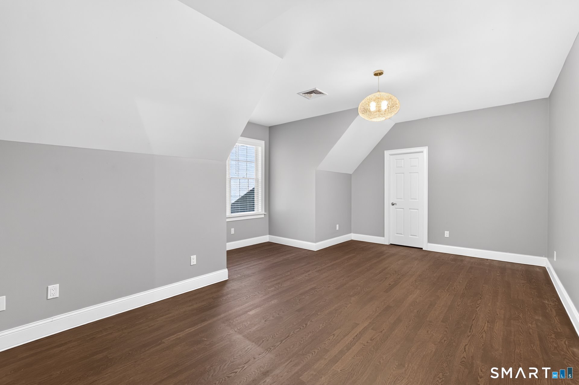 Empty upstairs bedroom with dark hardwood floors, gray walls, and a sloped ceiling.