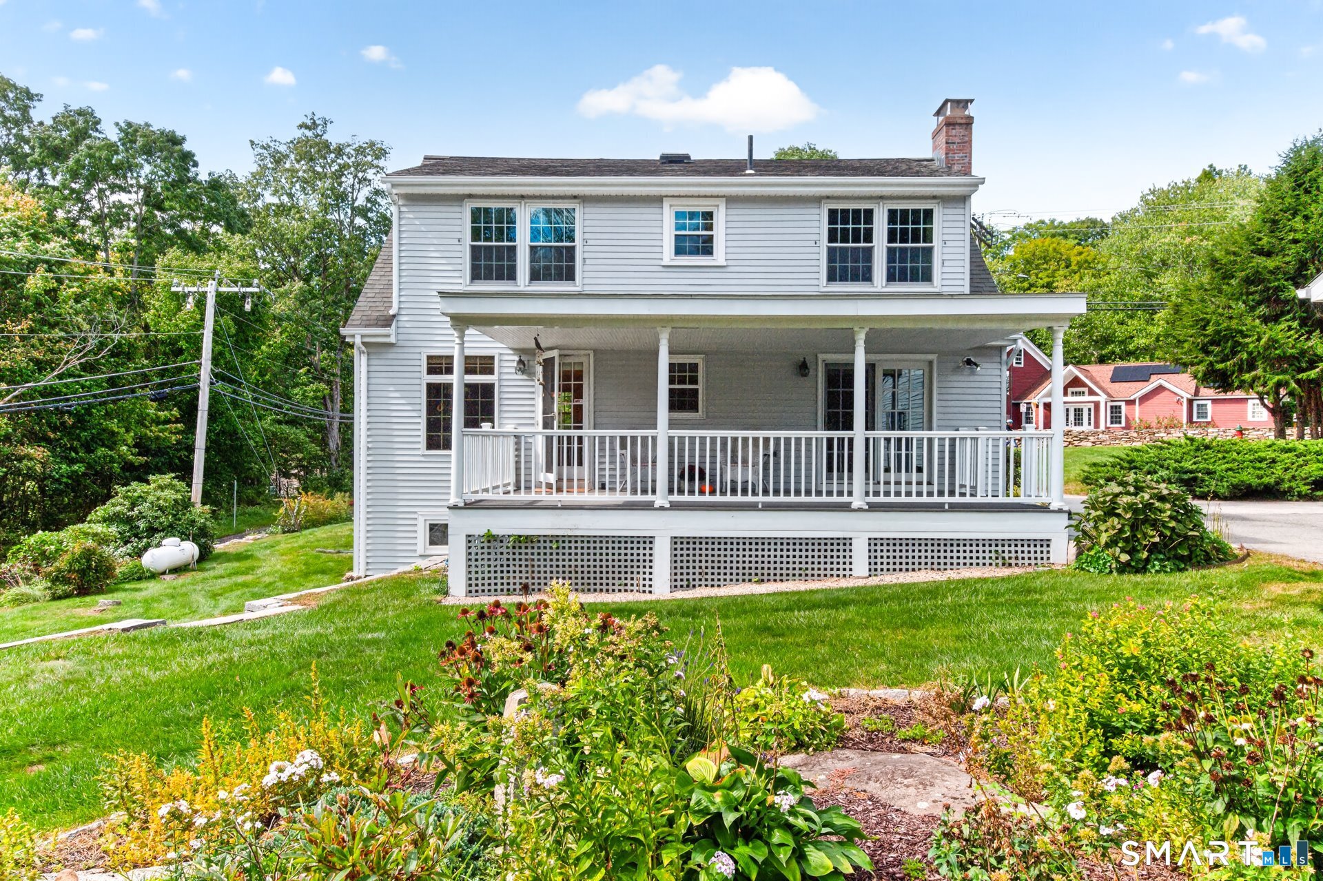 White two-story house with a broad covered porch overlooking a flower garden.