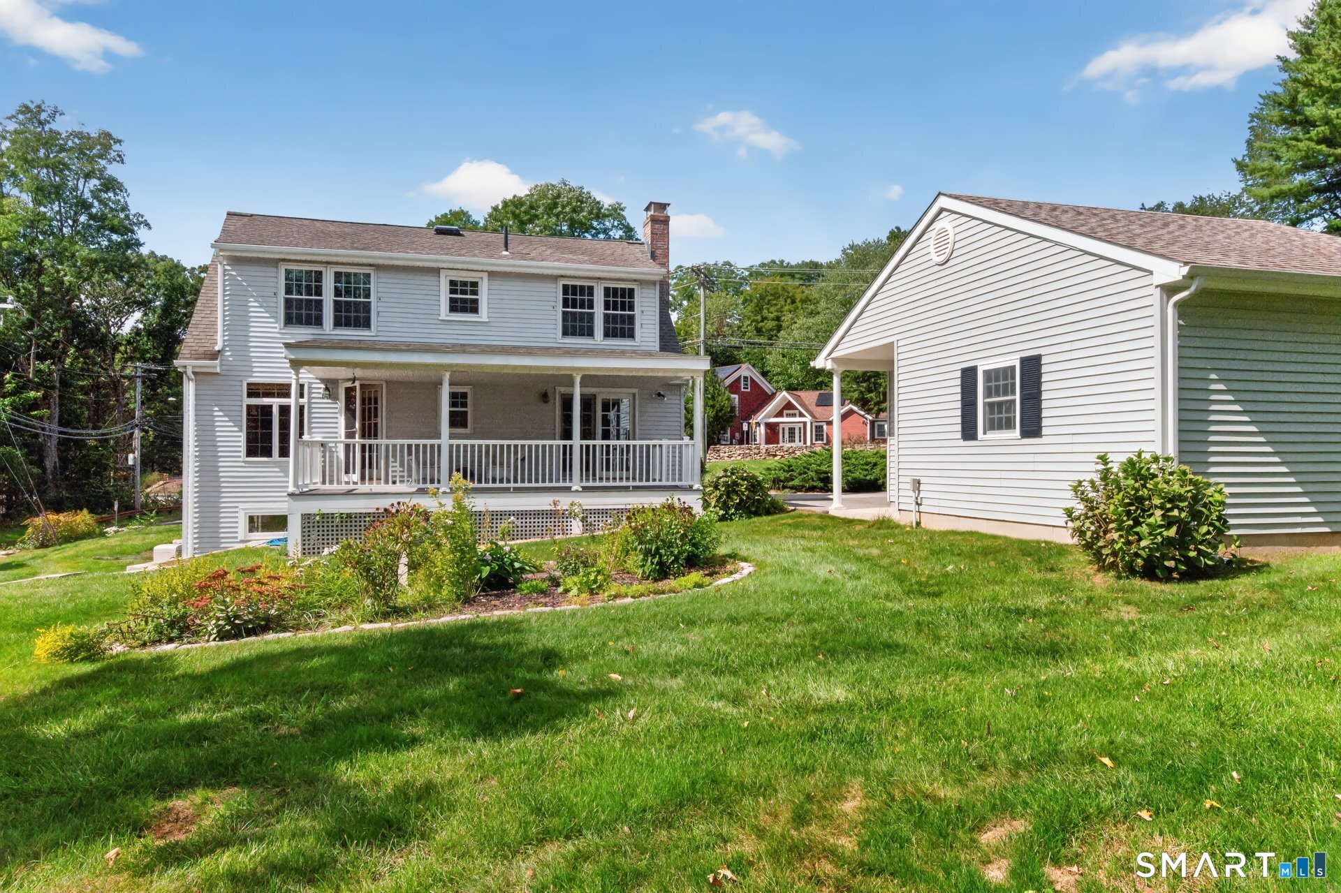 White-sided home with a covered porch, landscaped garden beds, and a broad green lawn.