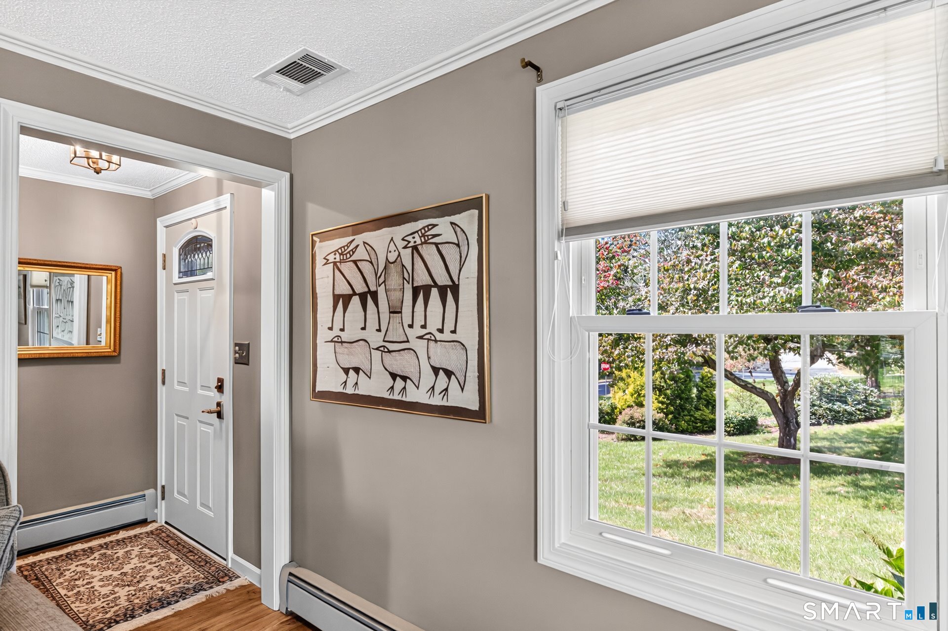 Entryway with a white front door, patterned rug, framed artwork, and a large window overlooking the yard.