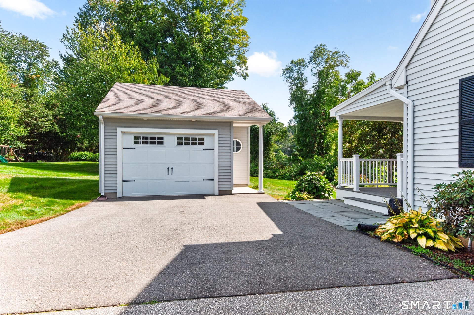 Detached gray garage and driveway beside a white-sided home with a covered porch.