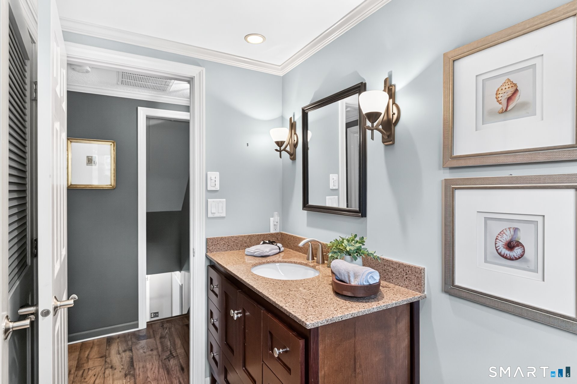 Bathroom vanity with a speckled countertop, dark wood cabinetry, wall mirror, and framed shell prints.