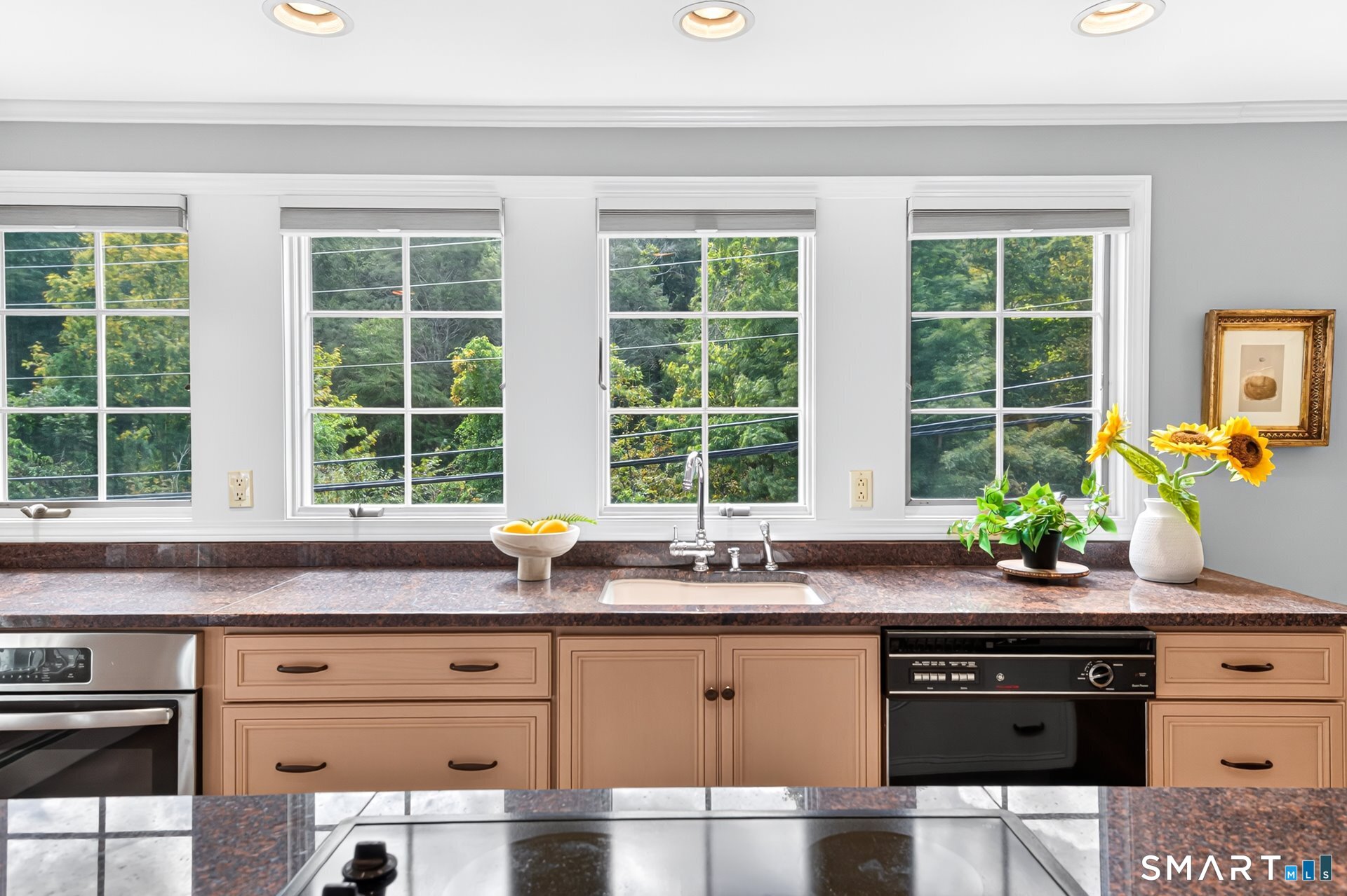 Kitchen with a wide row of windows above the sink and dark stone countertops.