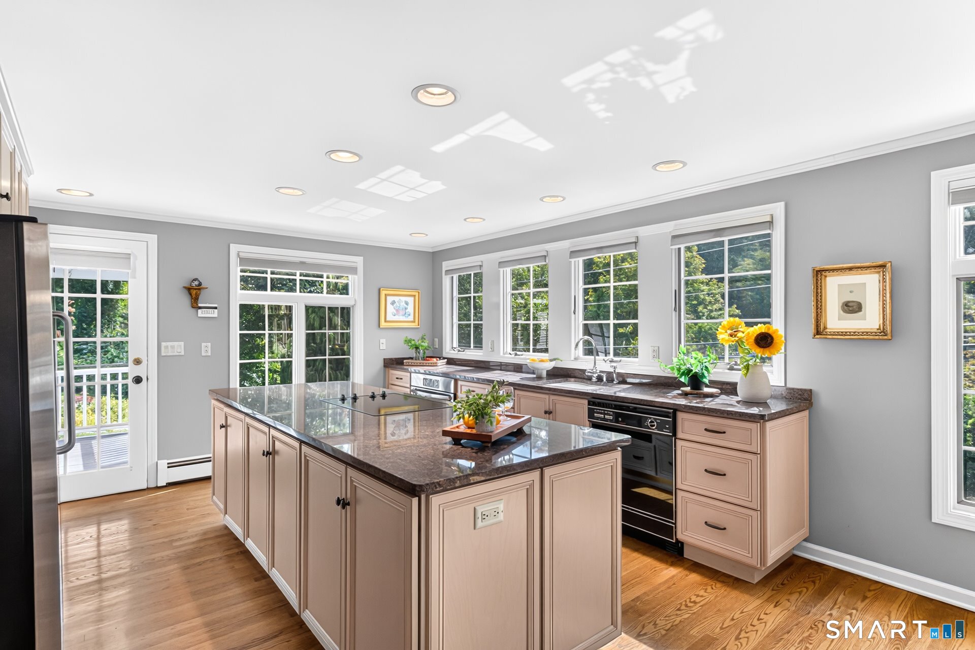 Bright kitchen with a large granite island, pale cabinetry, and windows overlooking greenery.