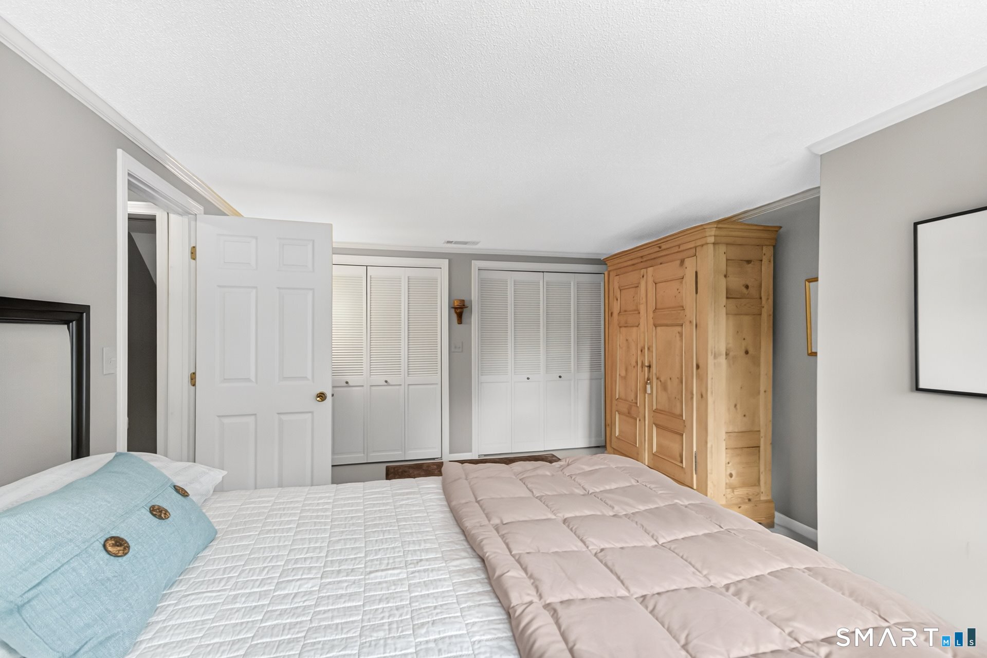 Bedroom with a quilted bed, louvered closets, and a large wooden armoire.