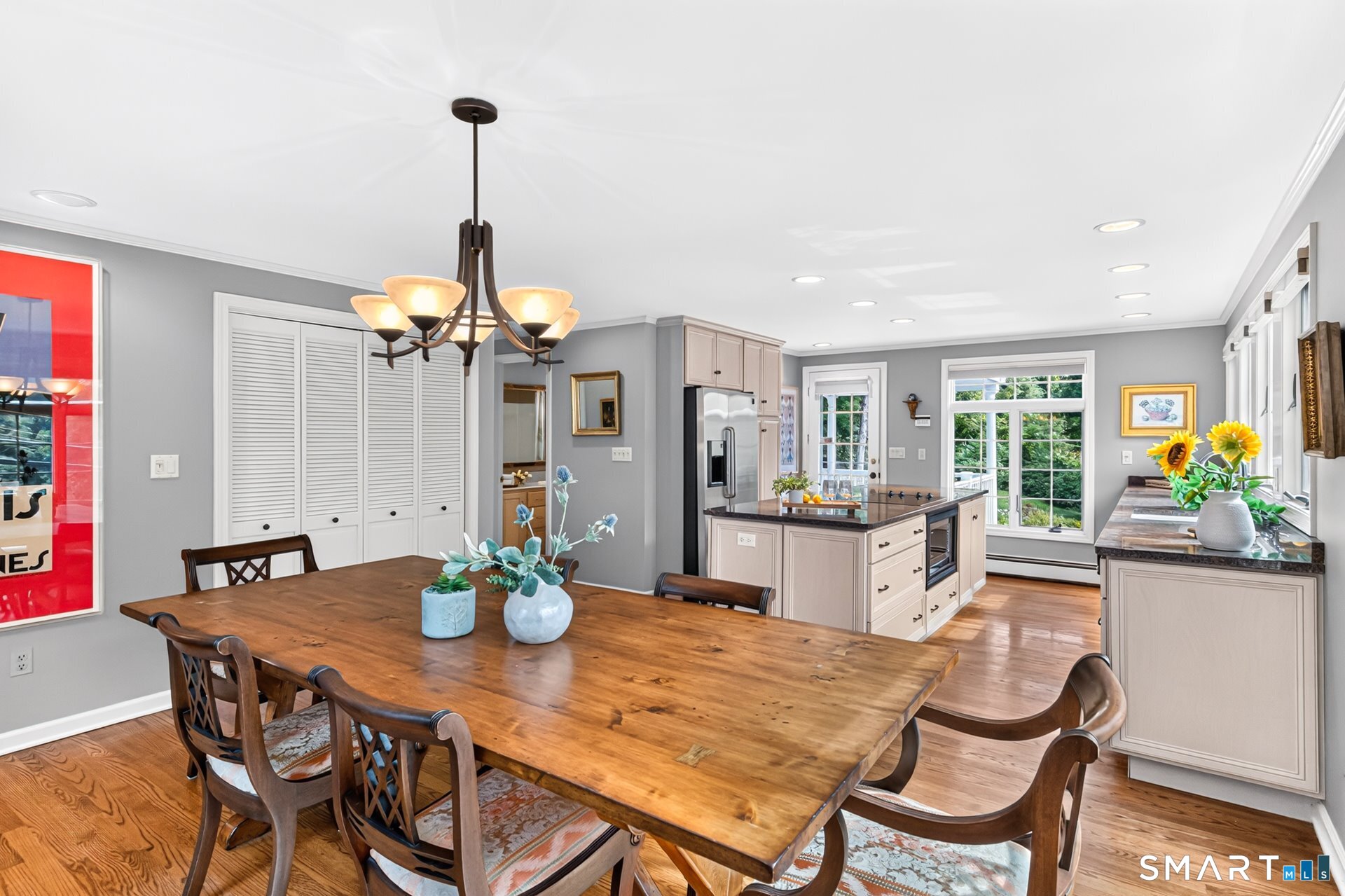 Kitchen and dining area with a large wooden table, central island, pale cabinetry, and hardwood floors.