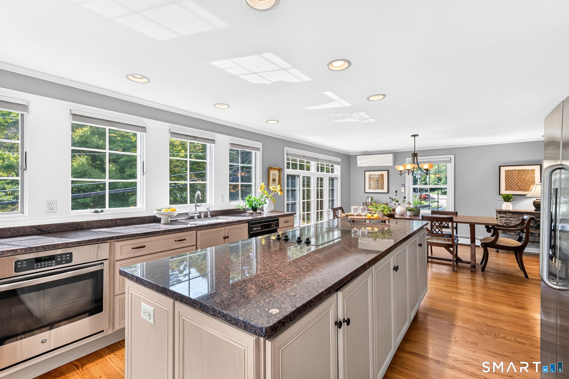Bright kitchen with a large granite island, stainless steel appliances, and windows overlooking greenery.