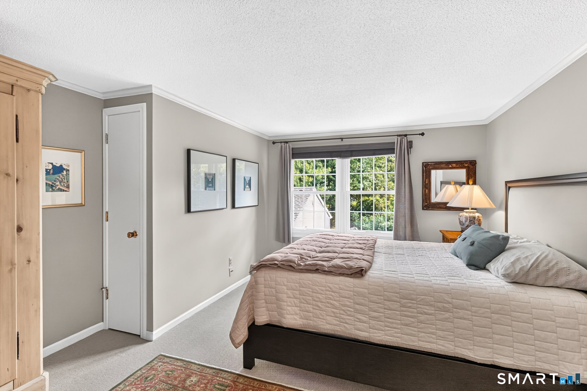 Bedroom with a large quilted bed, wood wardrobe, and window overlooking greenery.