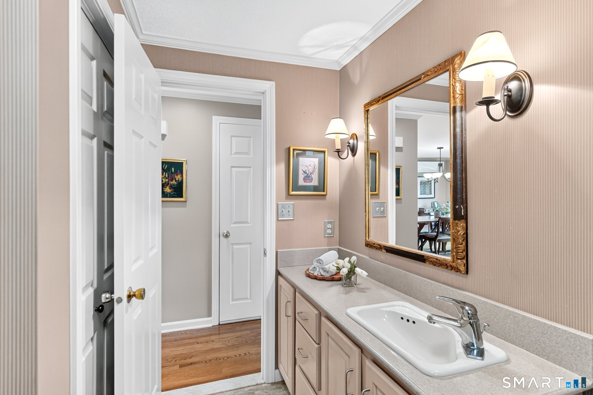 Bathroom vanity with a long countertop, white sink, ornate gold-framed mirror, and wall sconces.