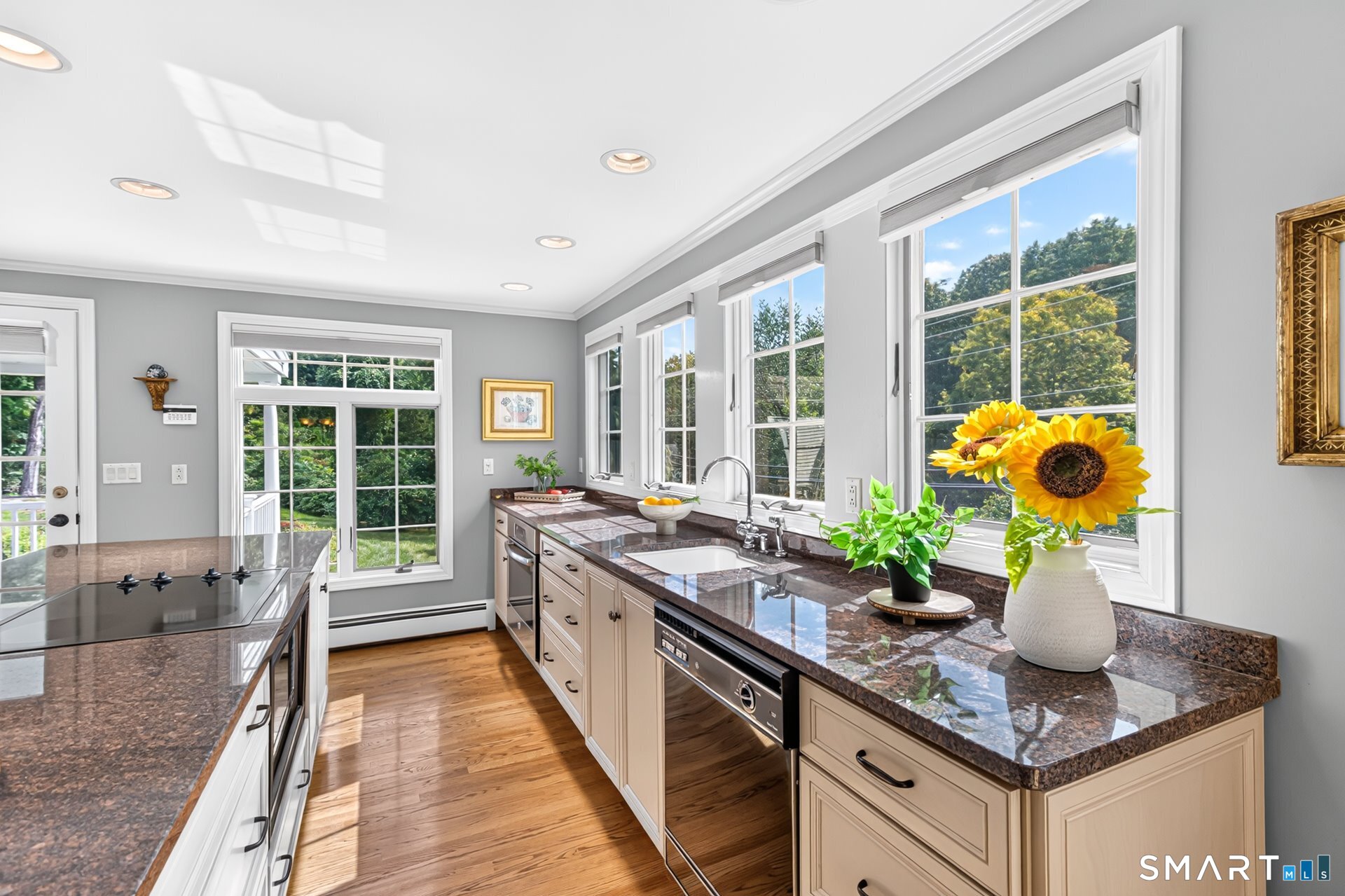 Bright kitchen with granite counters, pale cabinetry, hardwood floors, and large sunlit windows.