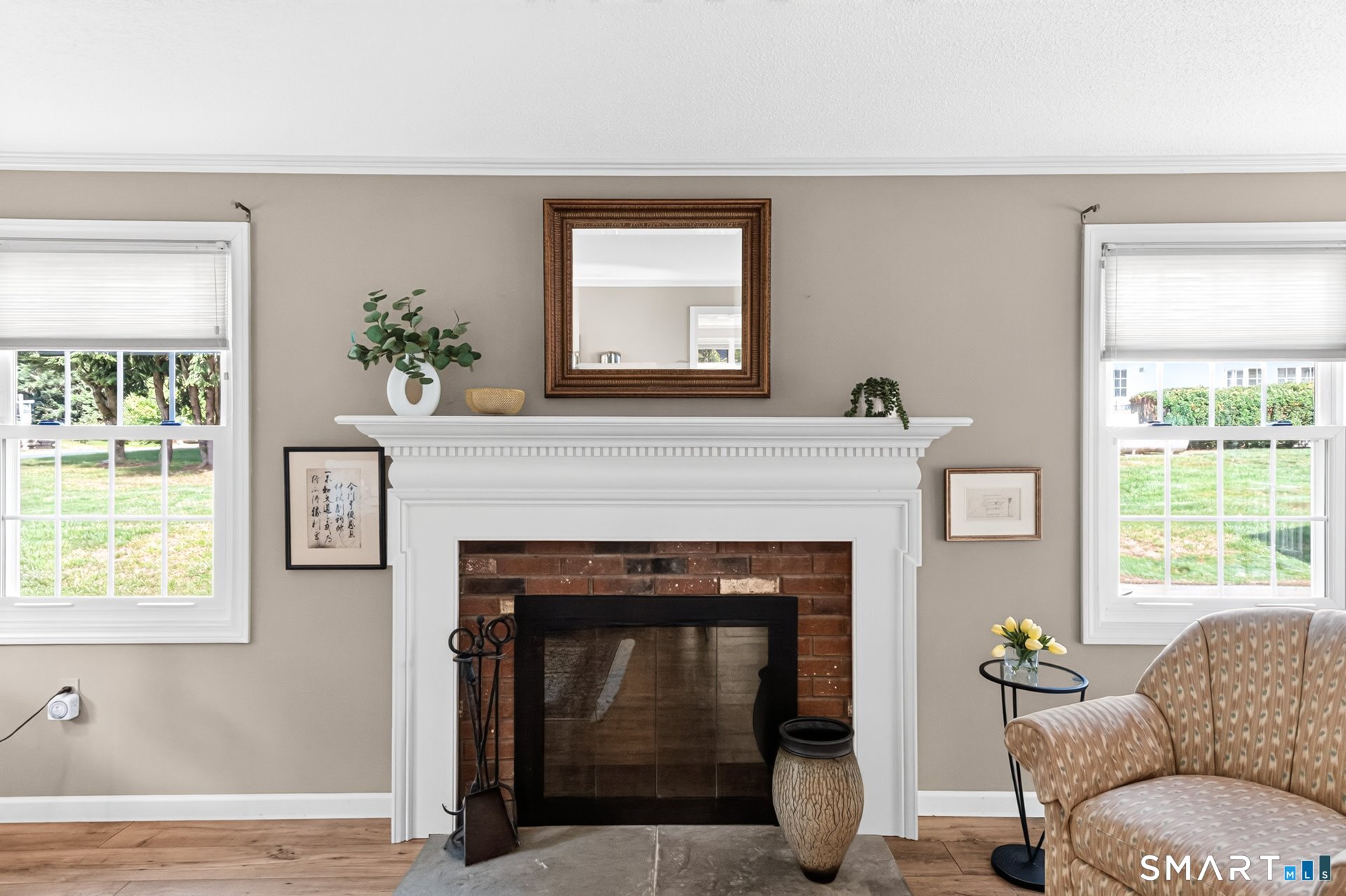 Living room with a brick fireplace, ornate white mantel, flanking windows, and patterned armchair.