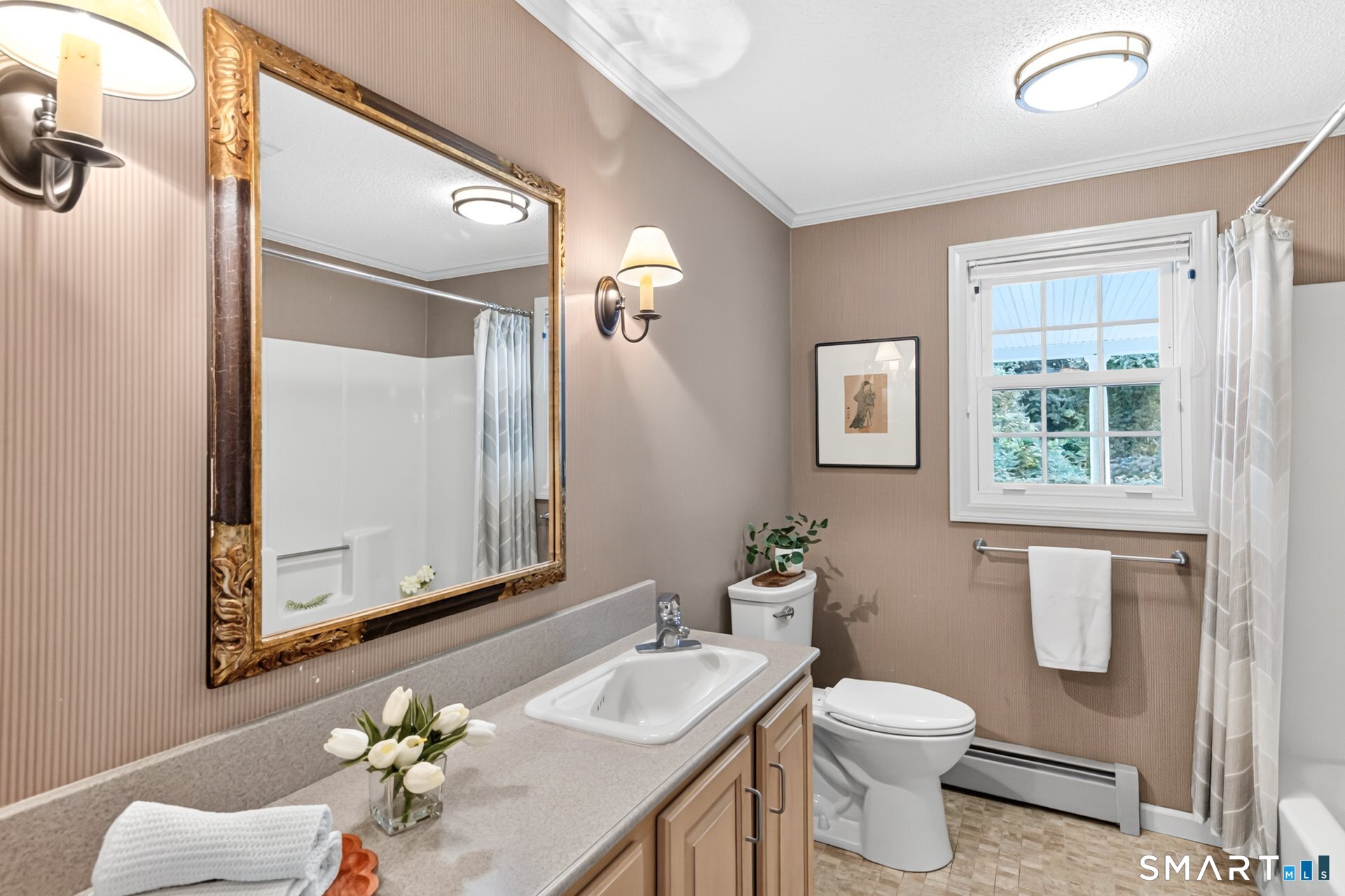 Bathroom with an ornate gold-framed mirror, long vanity, and window overlooking greenery.