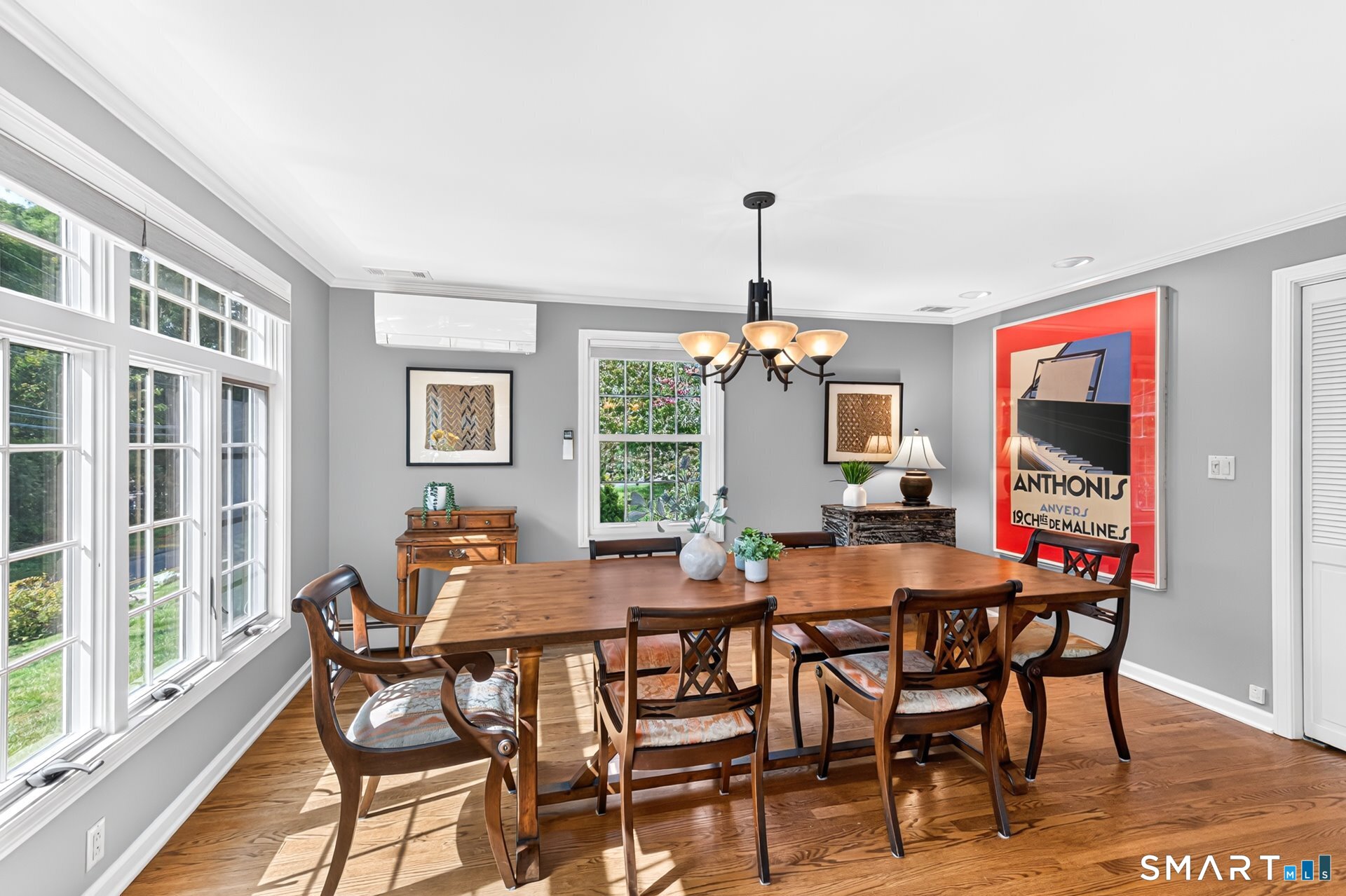 Dining room with a long wooden table, hardwood floors, large windows, and a chandelier.
