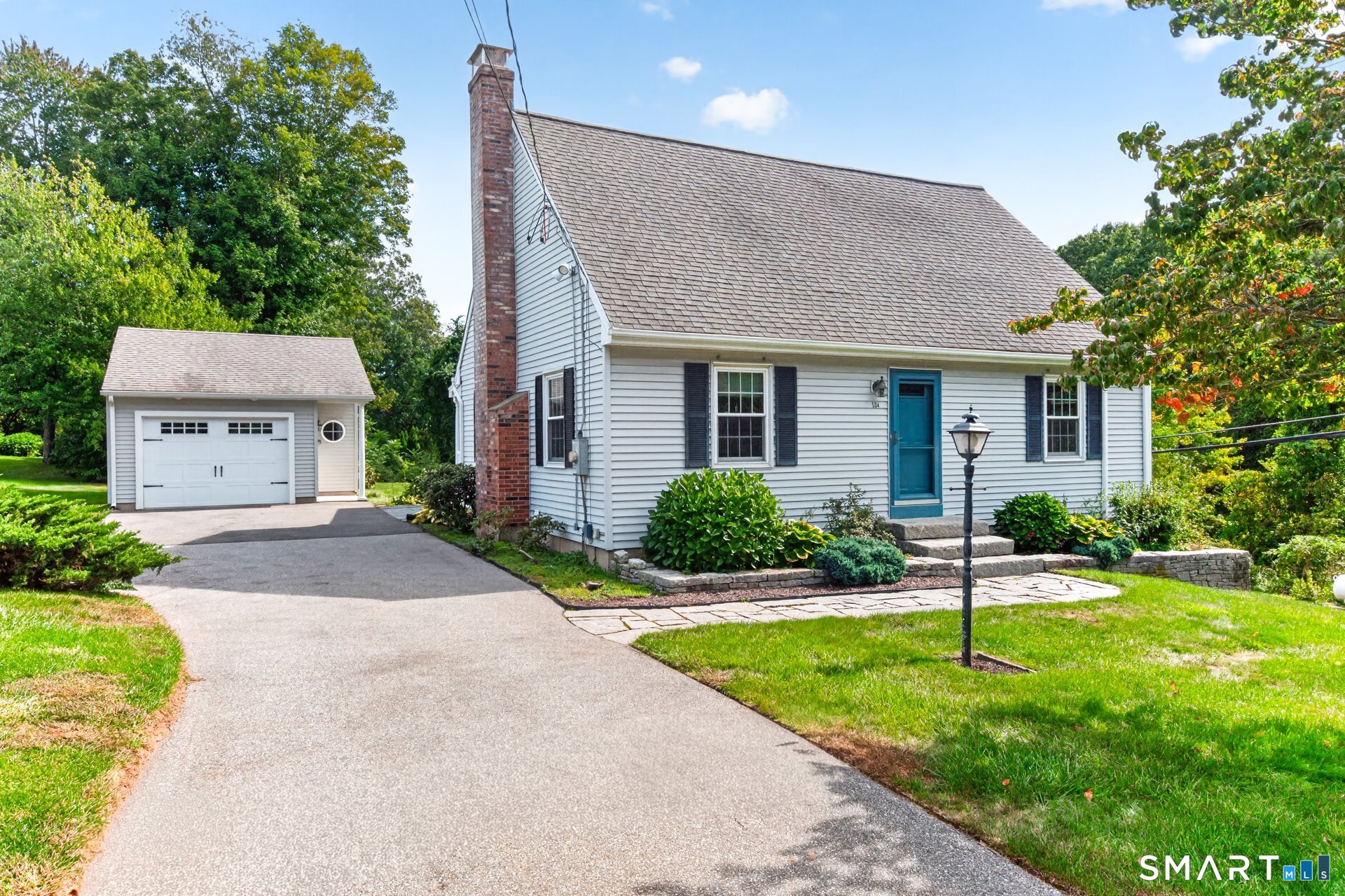 Light-gray house with a blue front door, brick chimney, detached garage, and paved driveway.